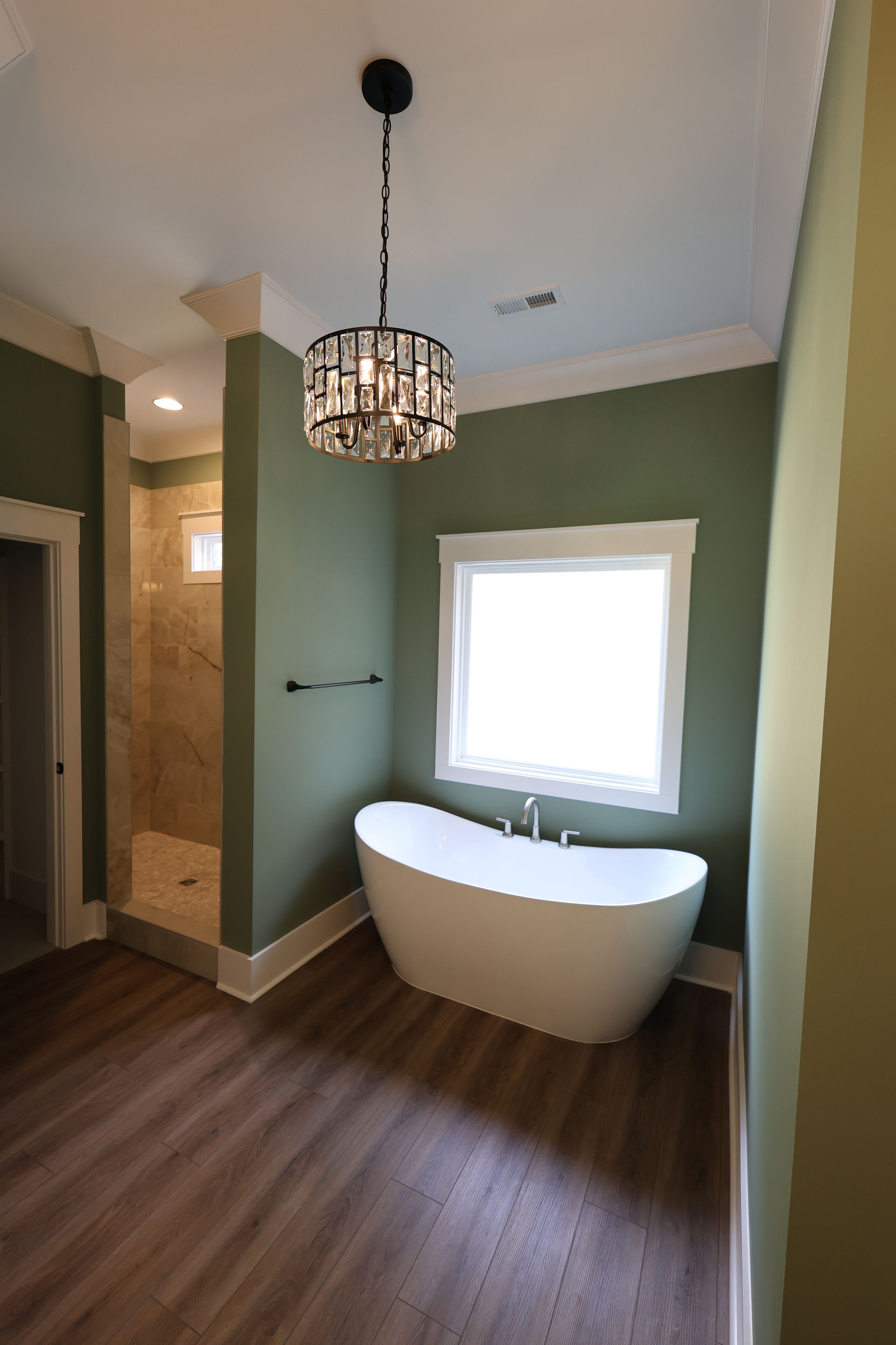 Bathroom with a white tub, walk-in shower, green walls, hardwood floor, and a crystal chandelier.