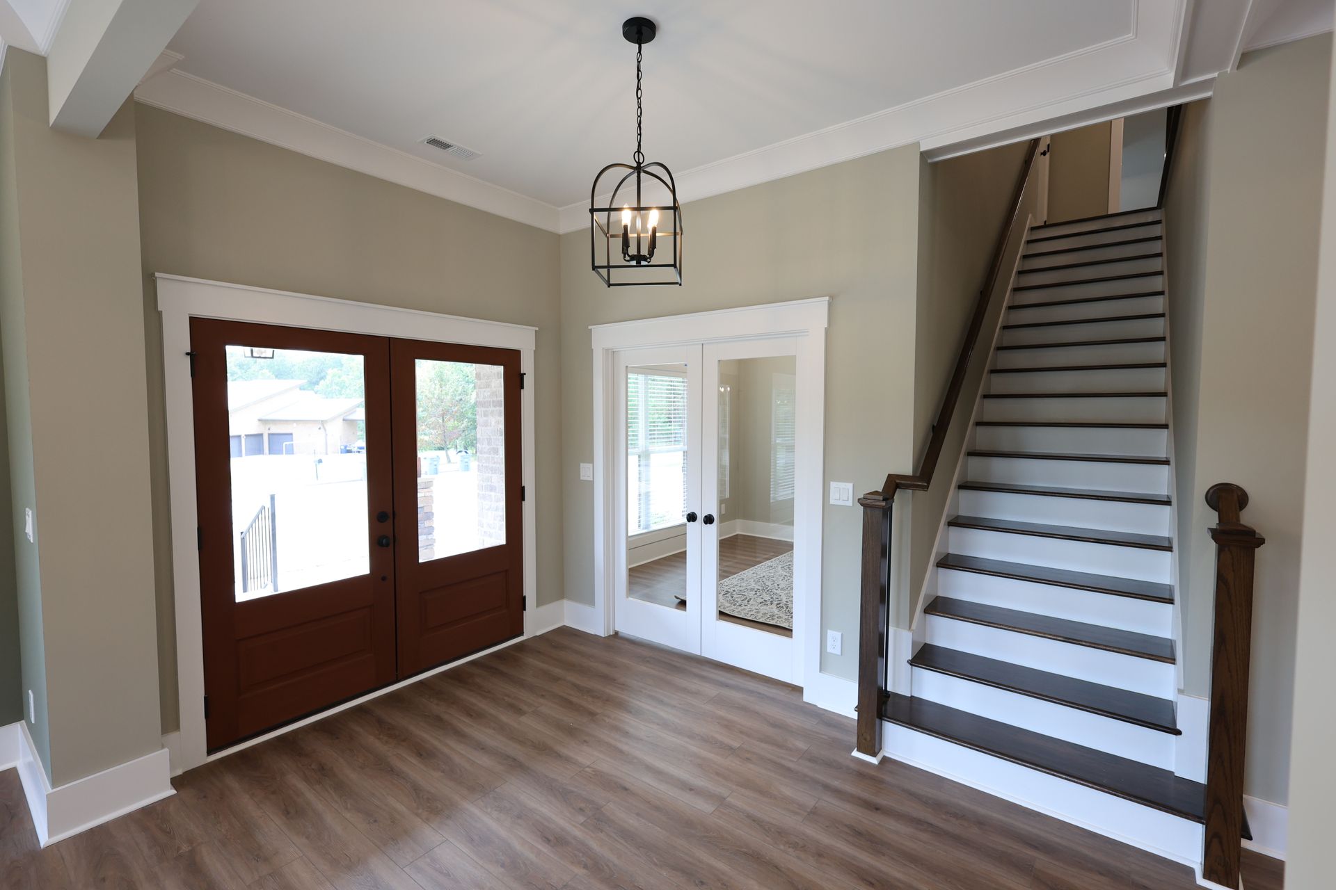 Entryway with brown doors, wood floors, and a staircase. Light fixture hangs from the ceiling.