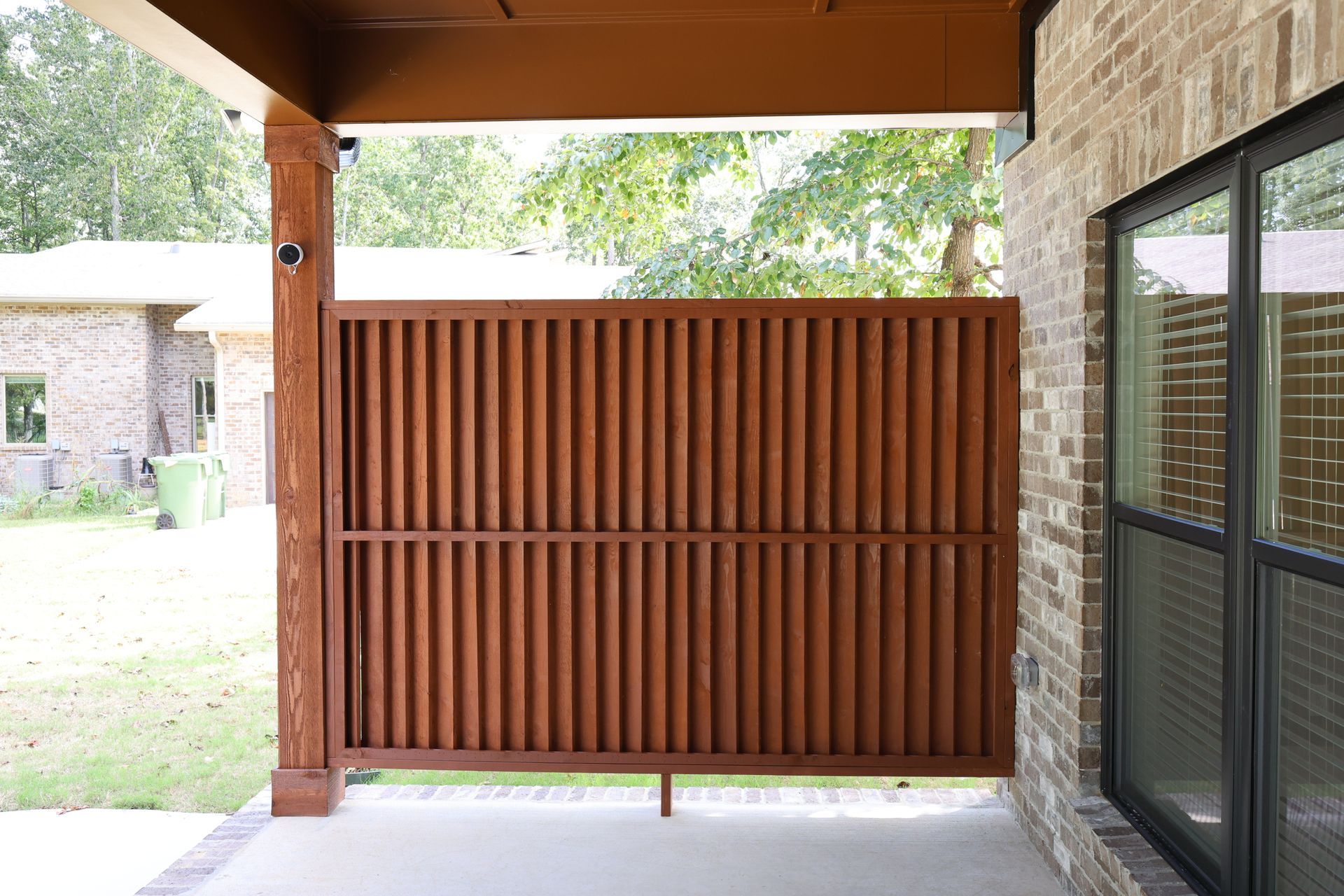 Brown vertical slatted privacy screen on a patio, adjacent to a brick wall and window.