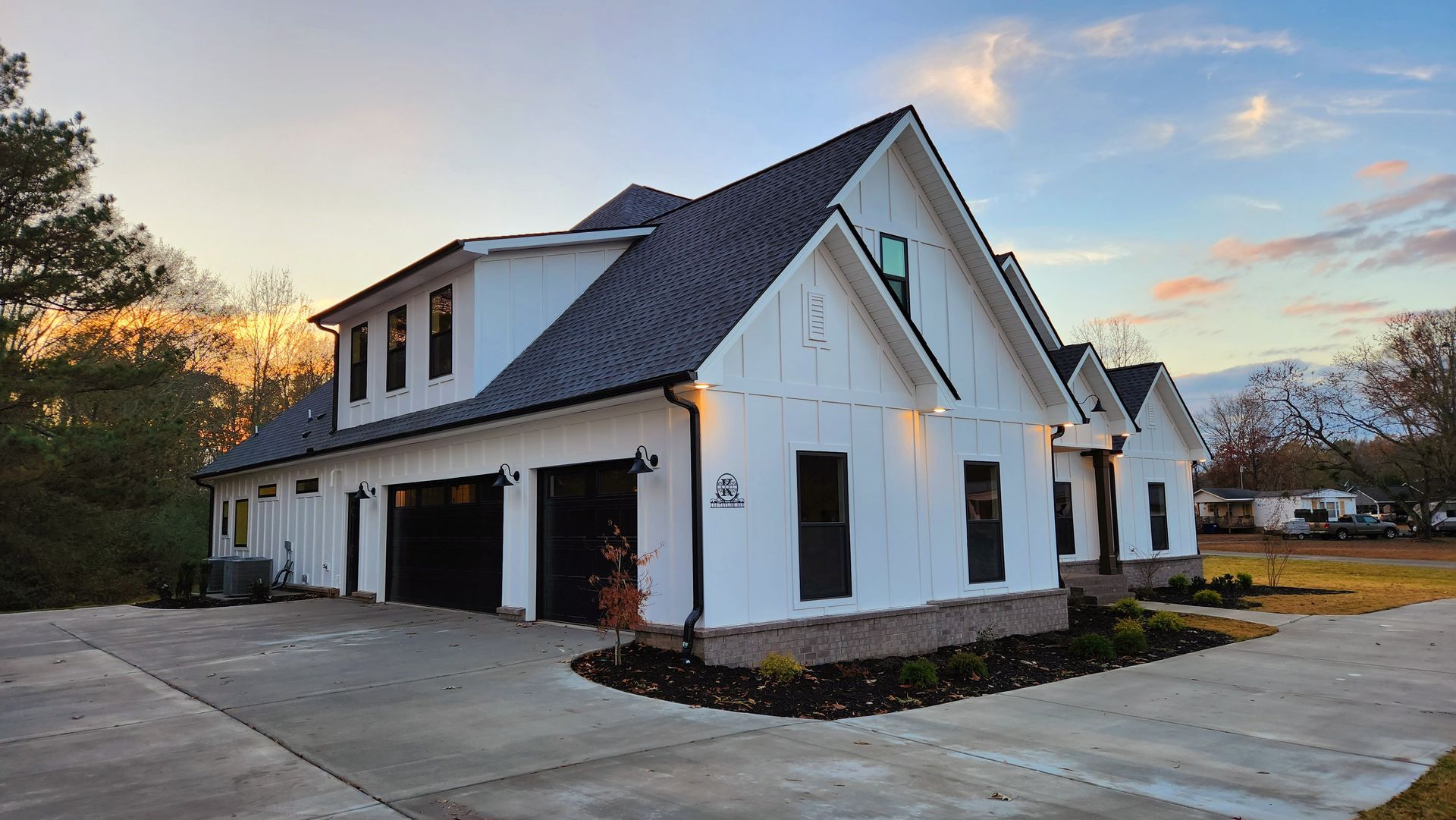 White farmhouse with black trim and garage doors, sitting on a concrete driveway under a cloudy sky.