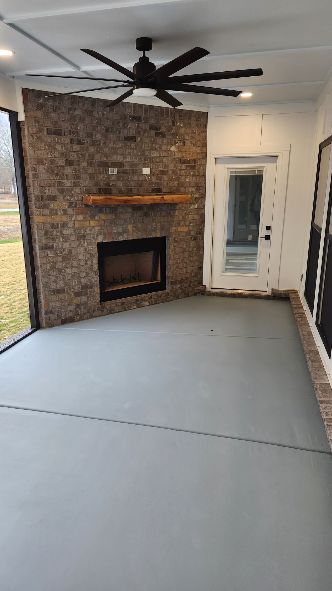 Enclosed patio with stone fireplace, gray floor, ceiling fan, and white door.