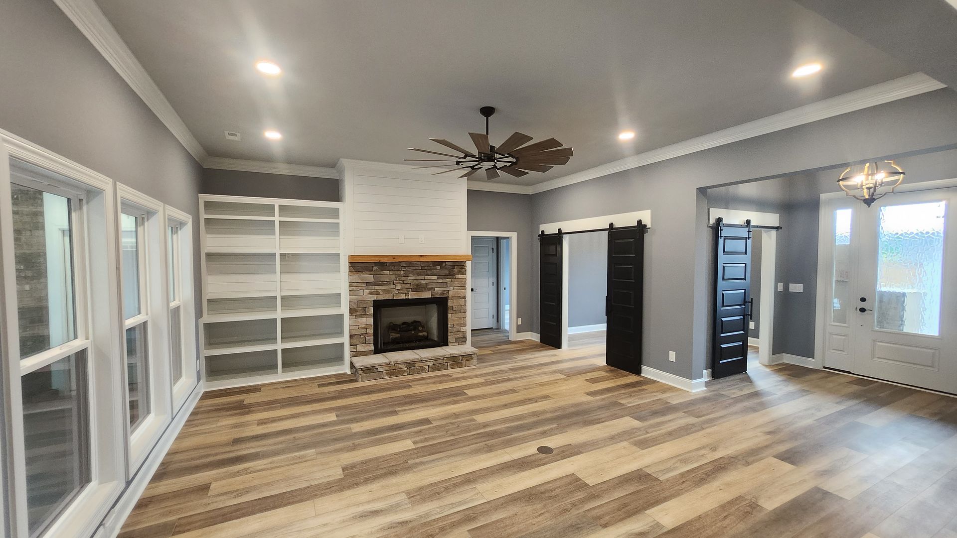 Living room with fireplace, built-in shelves, wood floors, sliding barn doors, and large windows.