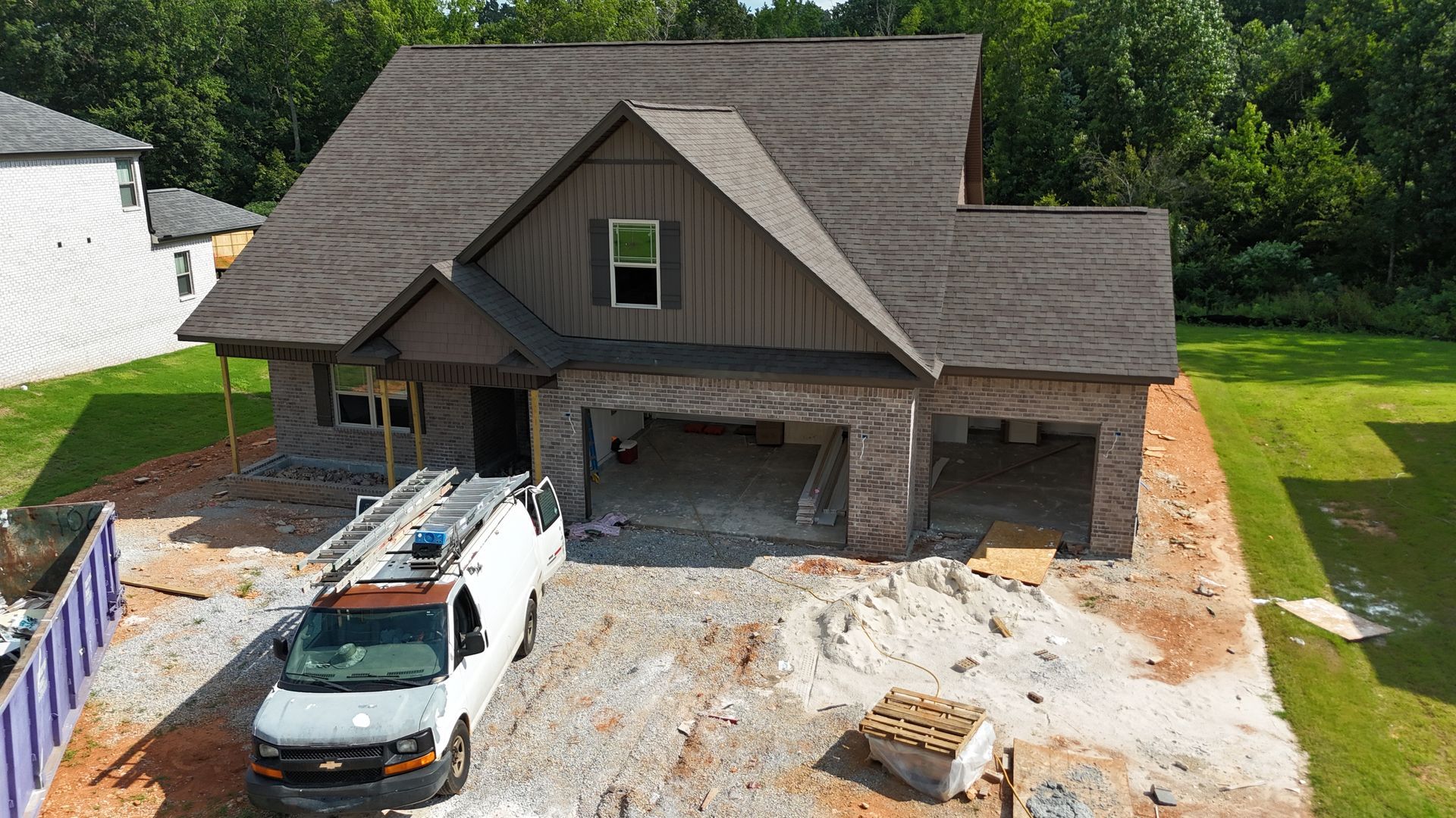House under construction with brick facade, gray roof, and white van parked in front.