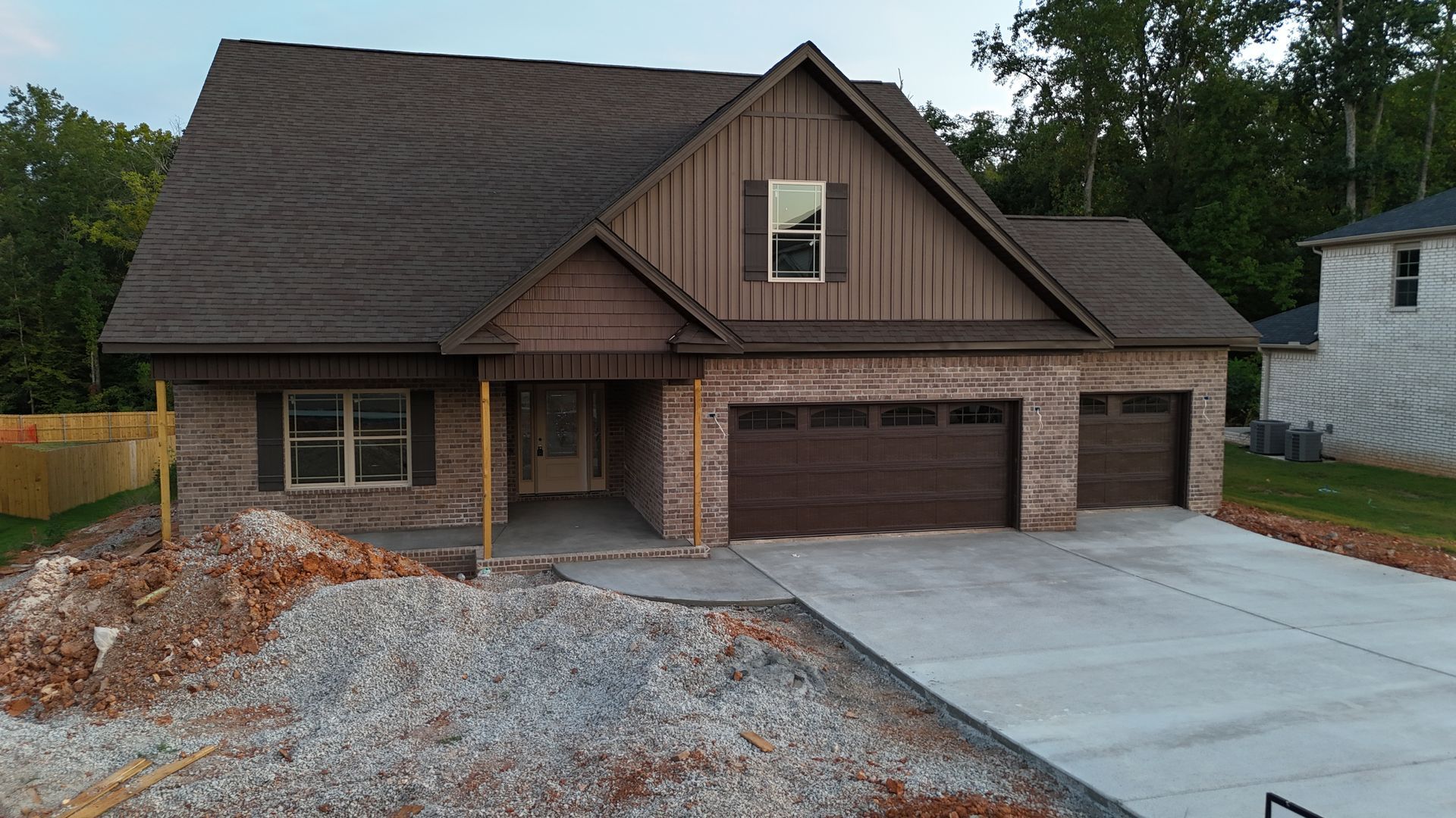 New brick house with brown roof and garage doors, construction site.