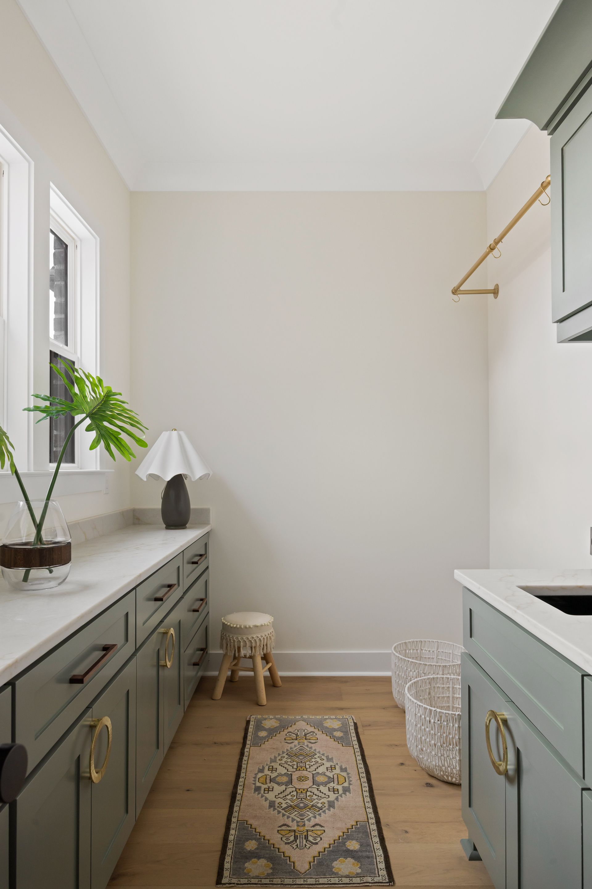 Laundry room with green cabinets, white countertops, a rug, and a clothing rod.