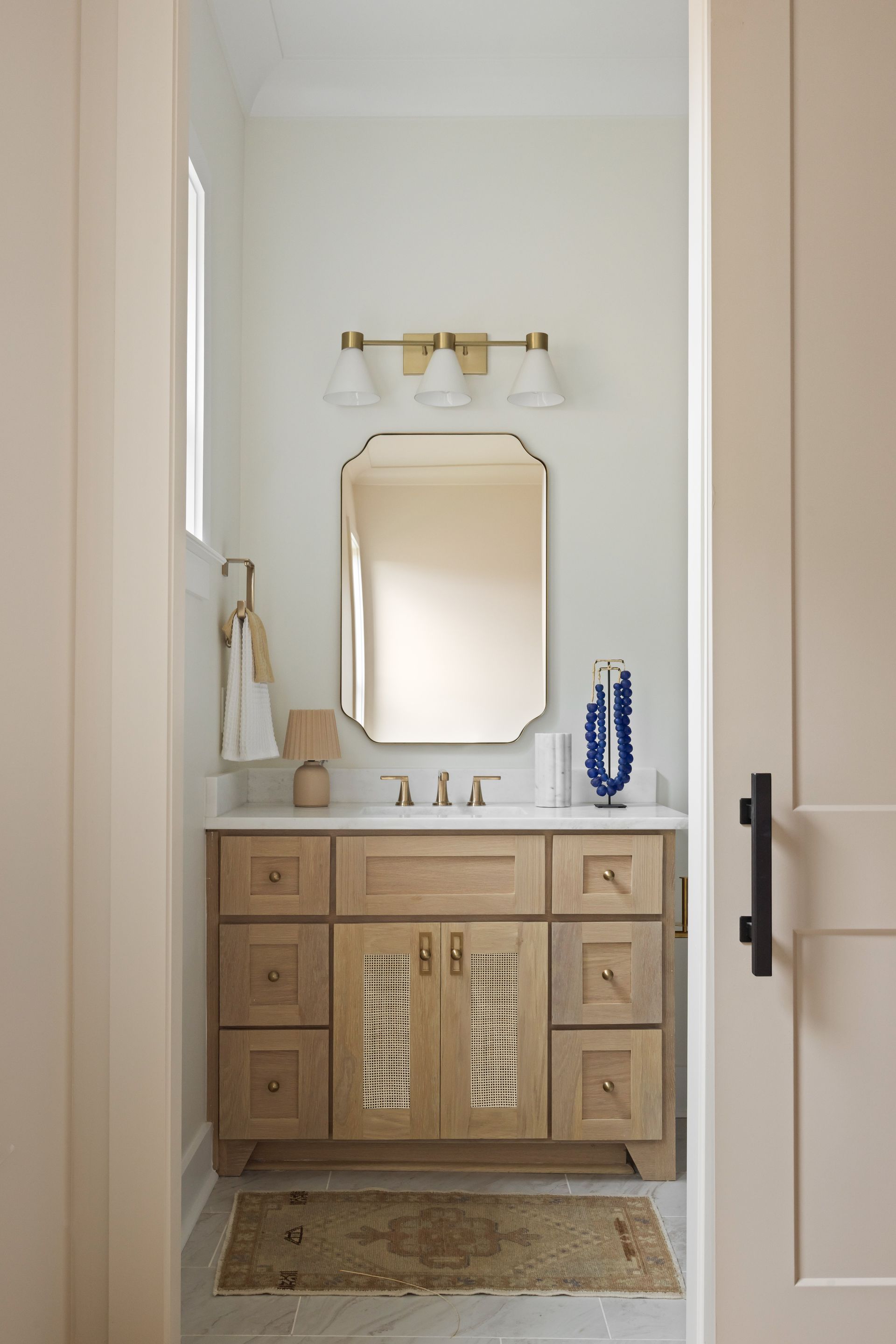 Bathroom with light wood vanity, decorative mirror, and brass light fixture.