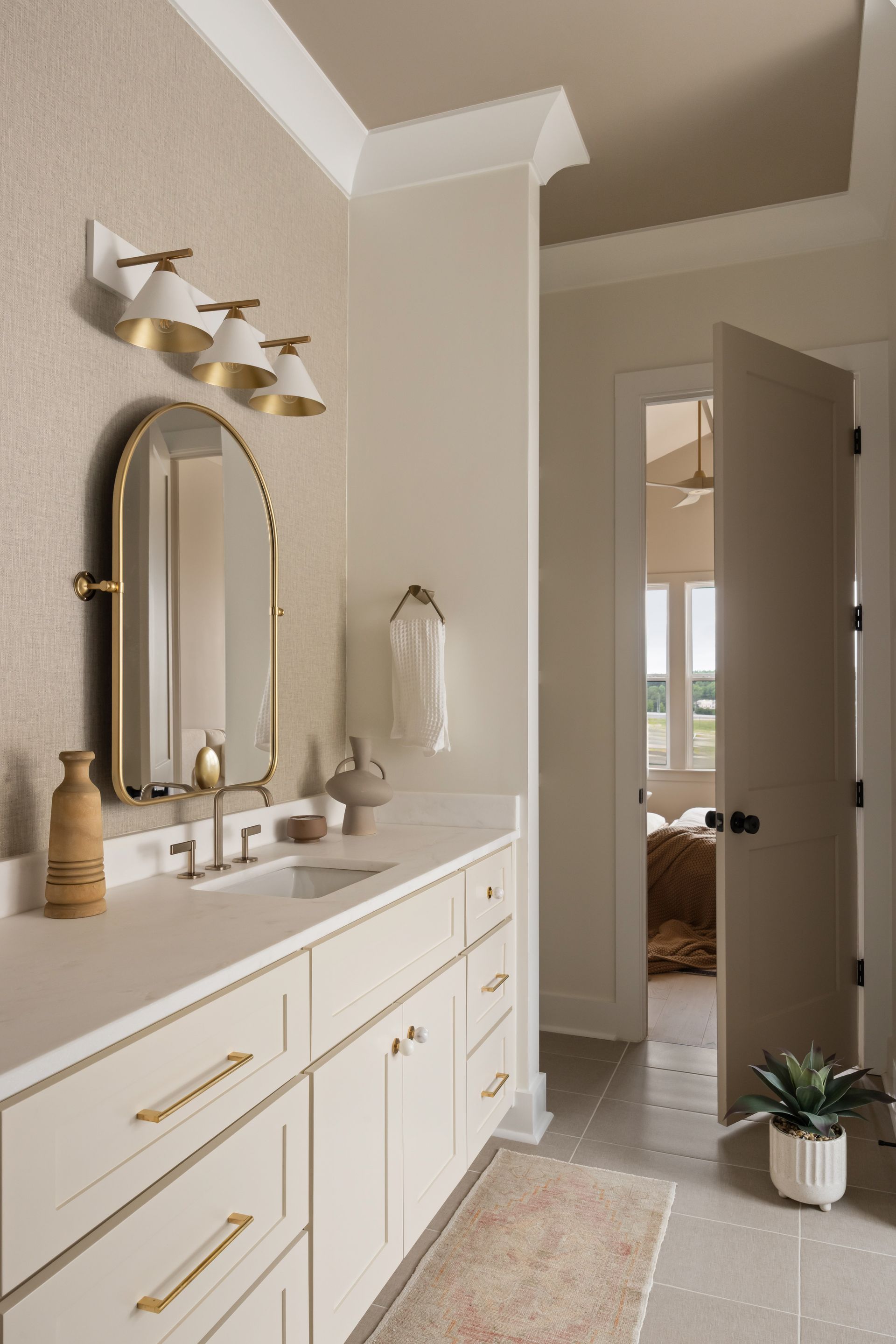 Bathroom with white vanity, gold accents, arched mirror, and open door to another room.