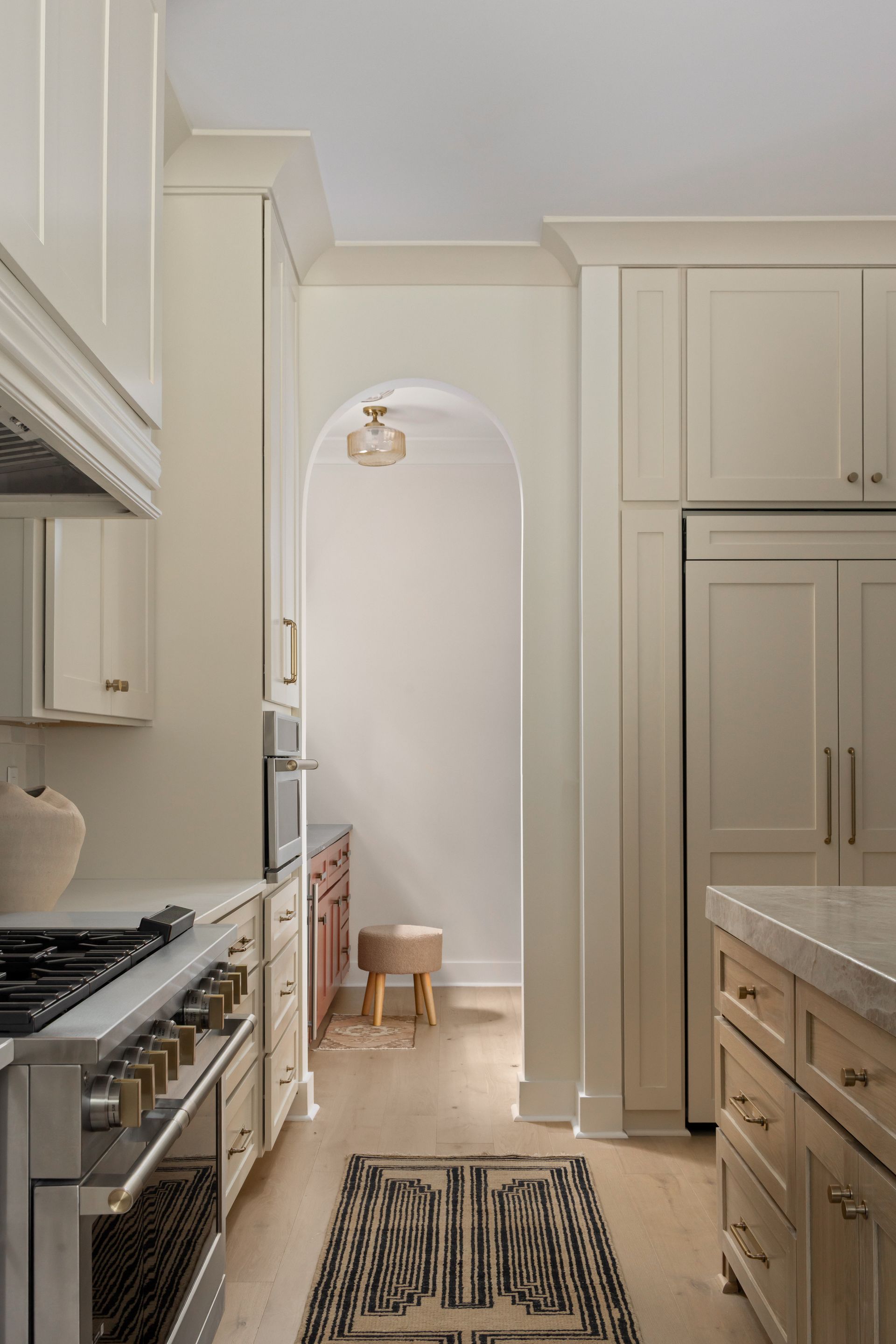 Kitchen with off-white cabinets, stainless steel appliances, and a hallway with a rug and stool.