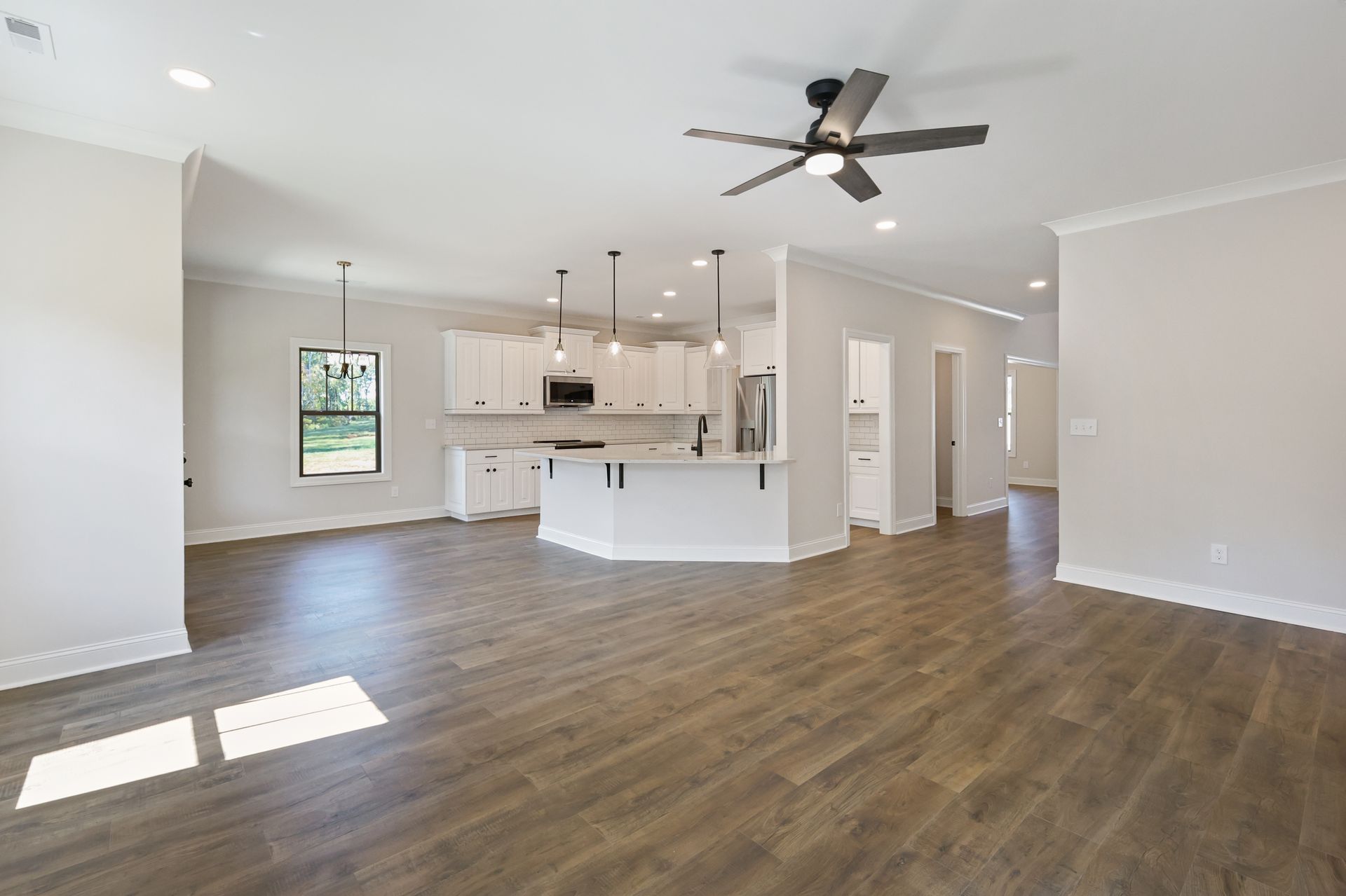 Open-concept living space with a kitchen, featuring white cabinetry, wood-look floors, and a ceiling fan.