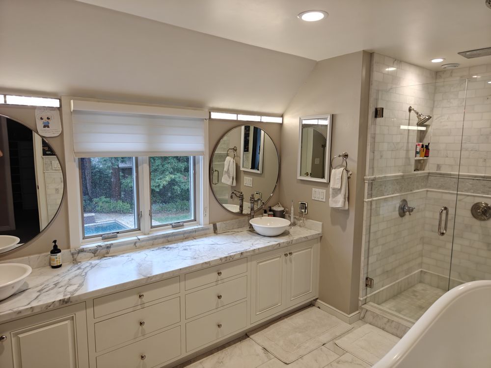 Bathroom with a white marble countertop, white cabinets, and a glass shower.