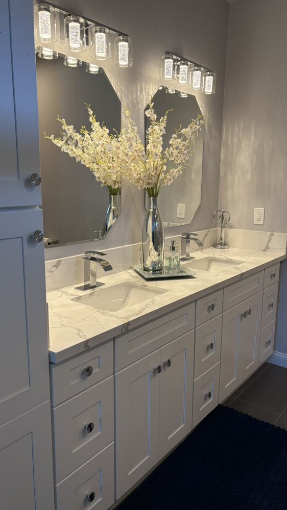 White bathroom vanity with marble countertop, mirrors, and floral arrangement.