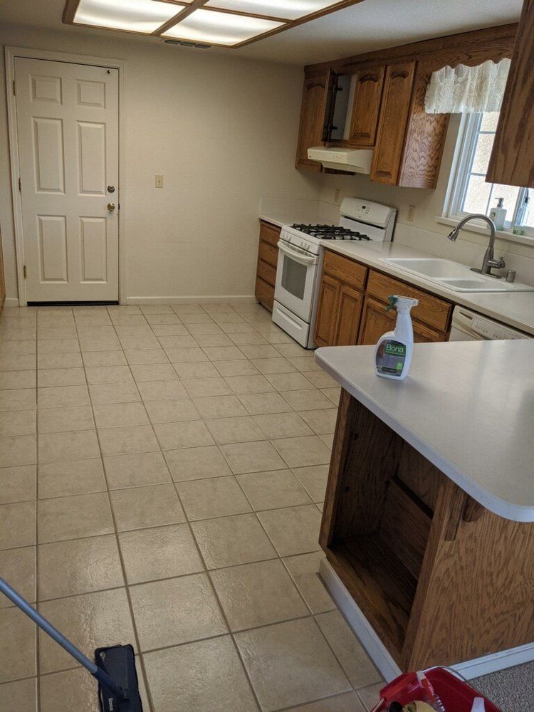 Kitchen with tile floor, light wood cabinets, white appliances, and a white counter with cleaning supplies.
