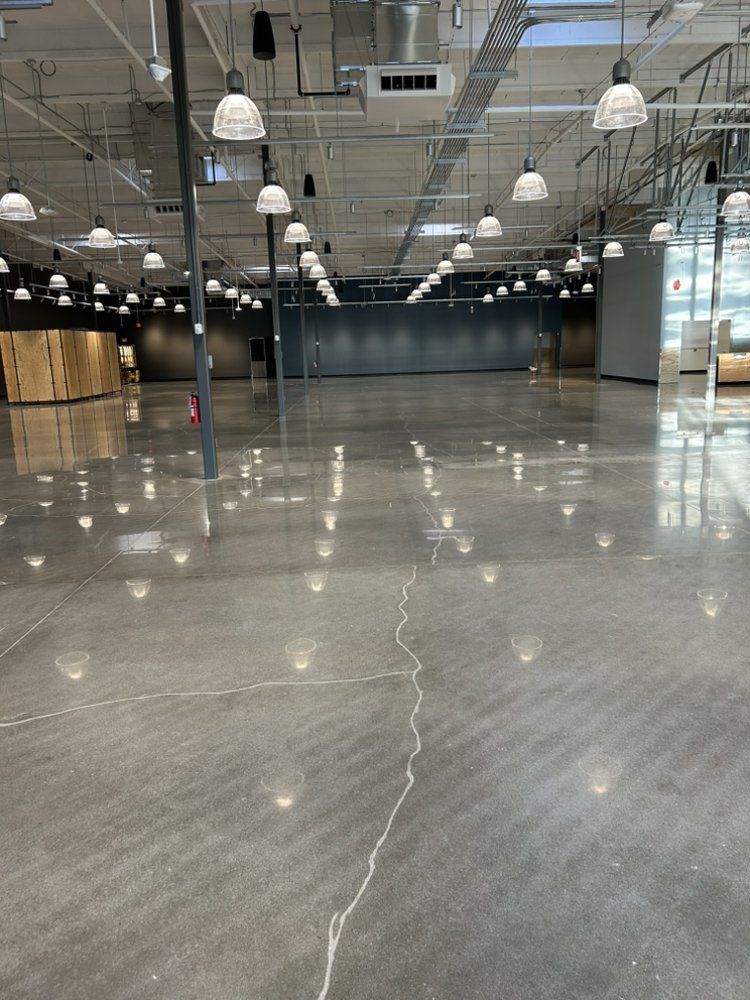 Large empty industrial space with polished concrete floor, overhead lights, and dark gray walls.
