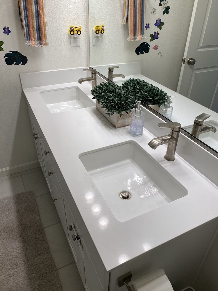 White bathroom vanity with two sinks, a mirror, and a small plant.