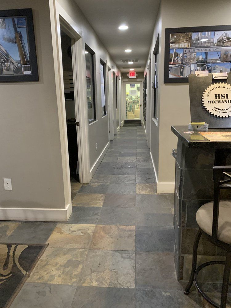 Long hallway with slate tile floor. Doors line both sides, some with artwork. Bar counter on right.