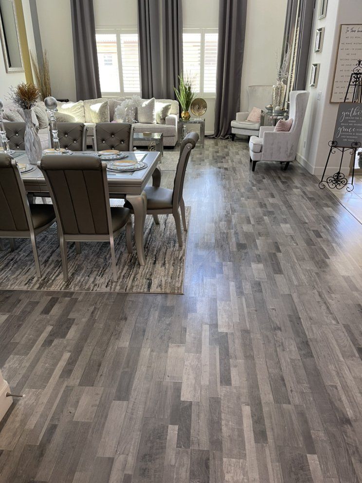 Gray wood-look floor in a light-filled living/dining area with furniture, curtains, and a table setting.