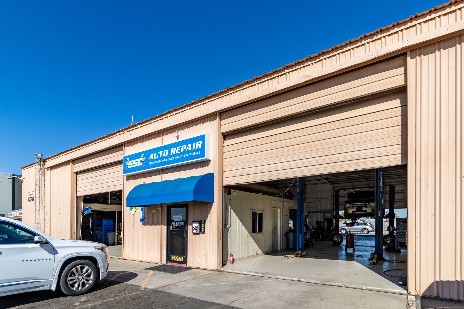Auto repair shop with open bays, blue awning, and a car in front.