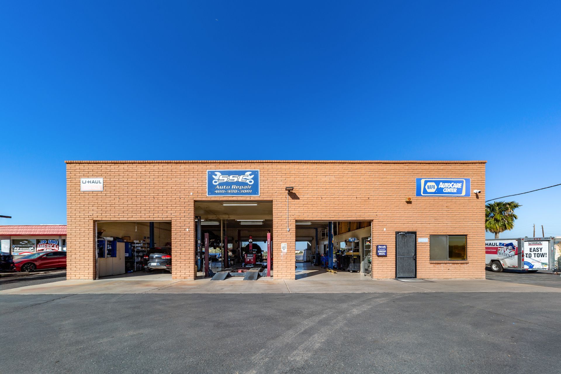 Brick auto repair shop with open bays, cars inside, and clear blue sky.