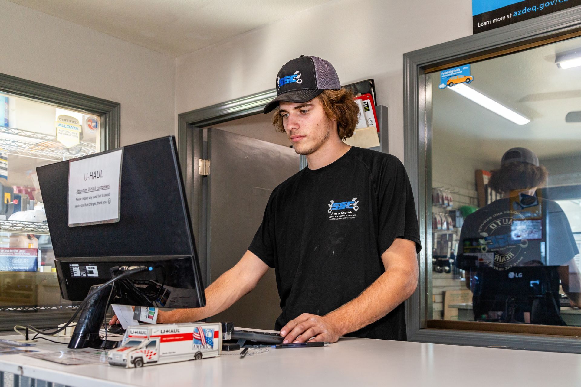 Person in black shirt and cap using a computer at a counter, possibly in a store.