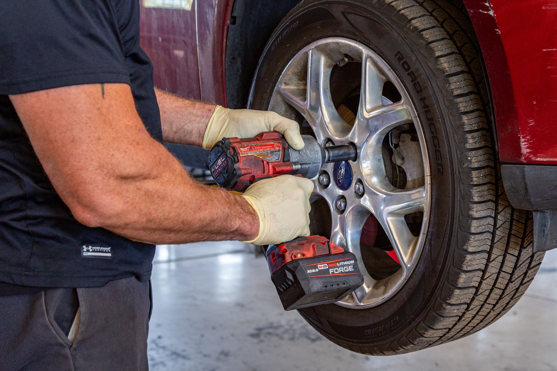 Person using a power tool to remove a car tire in a garage setting.