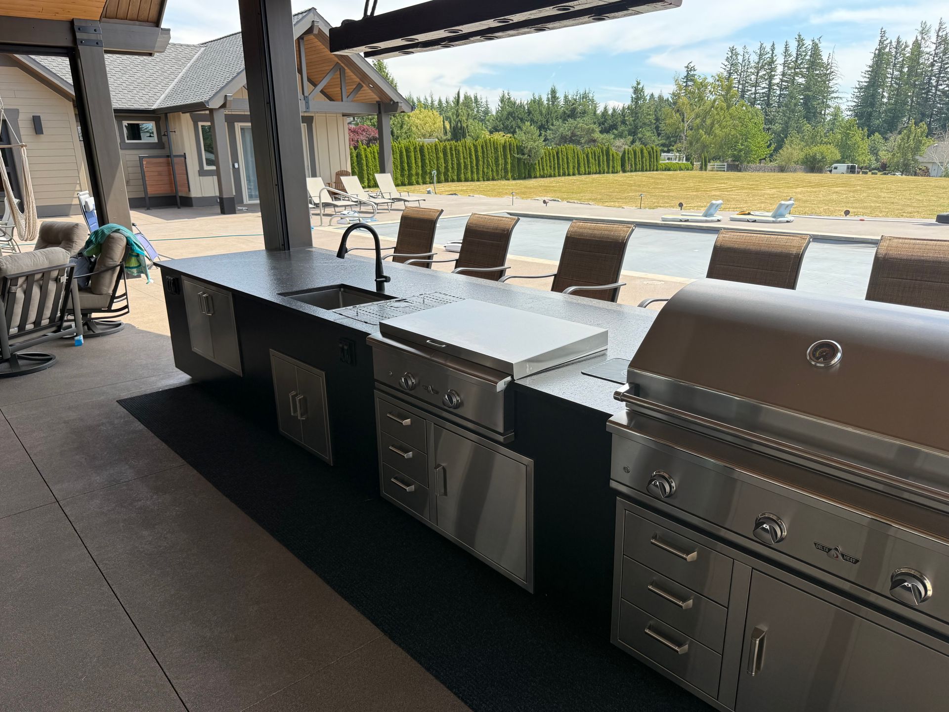 Outdoor kitchen with built-in grill and stainless steel countertops overlooking pool in Washougal, WA custom home