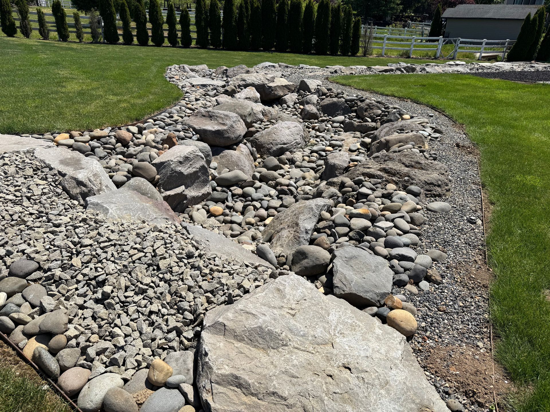 Natural river rock drainage swale with boulder landscaping in Washougal, WA backyard