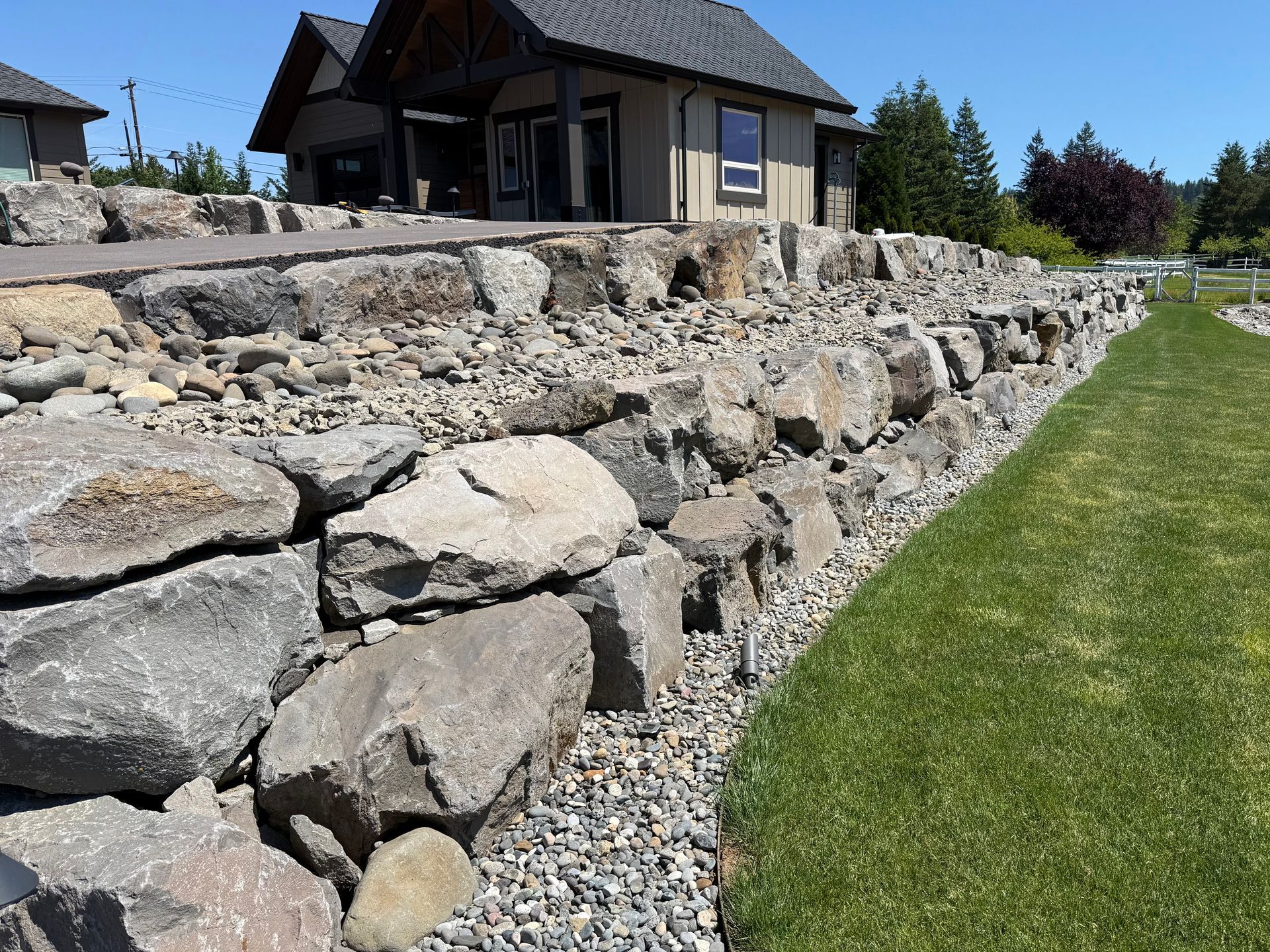 Large boulder retaining wall with river rock landscaping by Elite Construction & Design in Washougal, WA