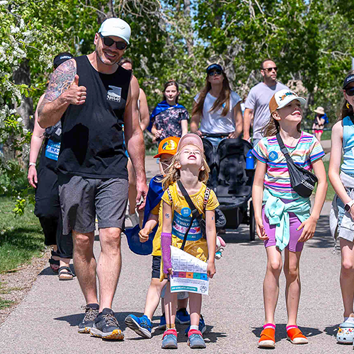 Un père faisant un « pouce en l’air » pendant qu’il marche avec ses deux filles sur le parcours de l’événement.