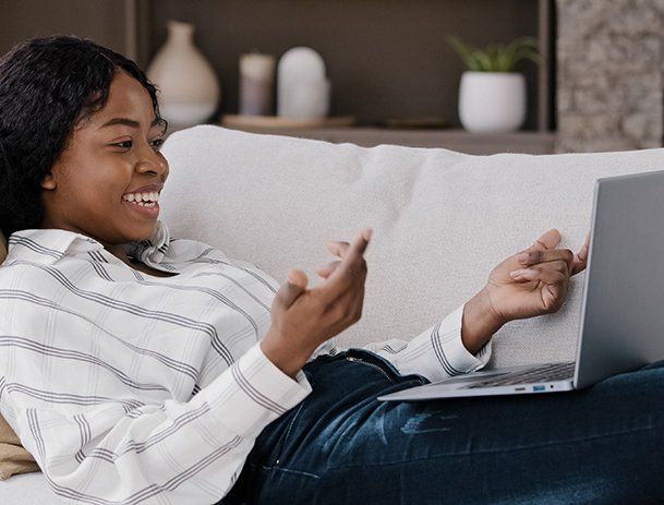 Woman lying on her couch engaging in an online event on her laptop