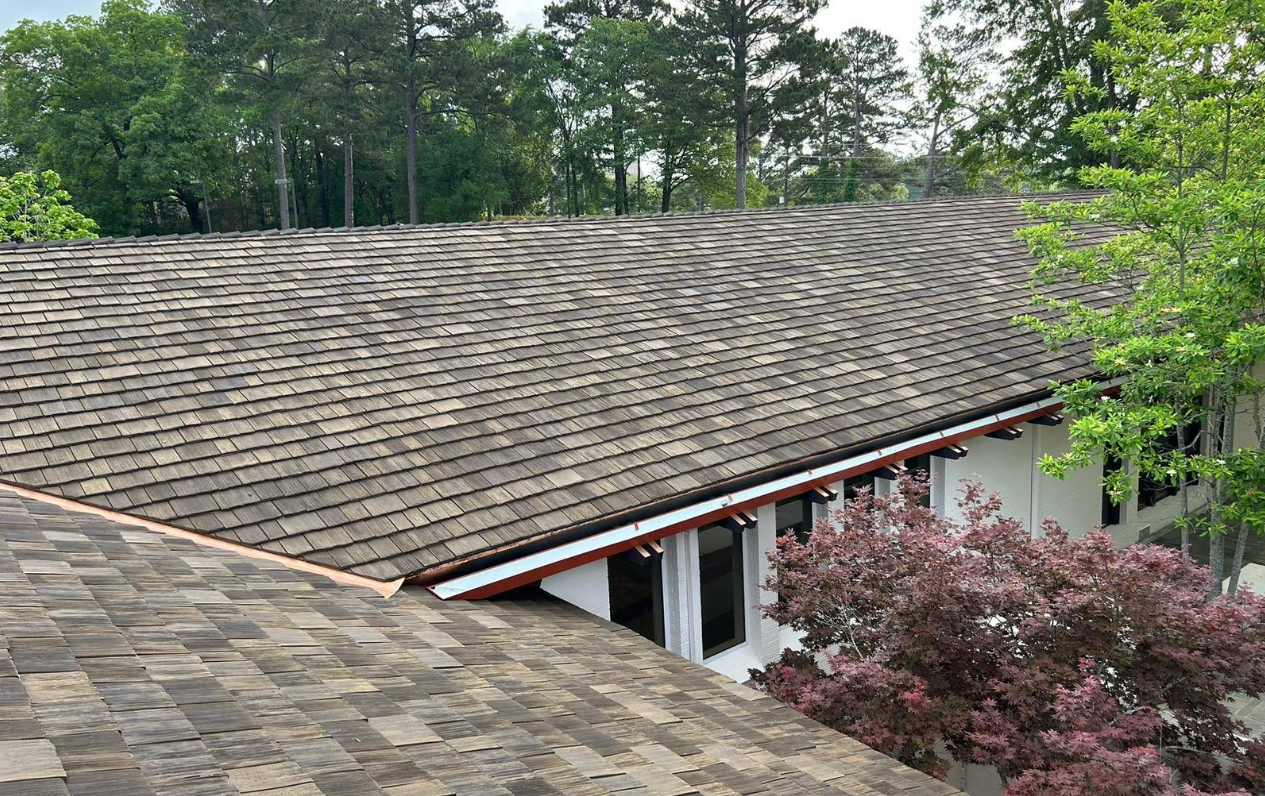 Dark shingle roof, possibly weathered, of a building with trees in the background.