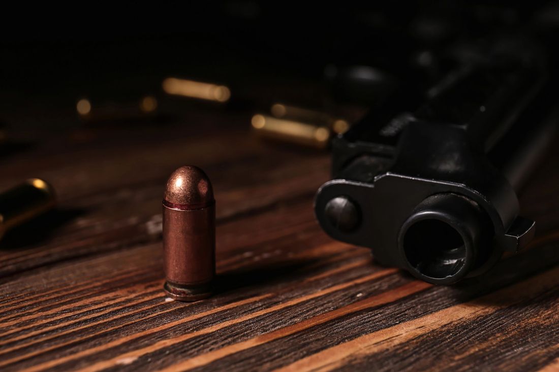 Un proiettile di rame è appoggiato su un tavolo di legno accanto a una pistola nera, con proiettili sfocati sullo sfondo.