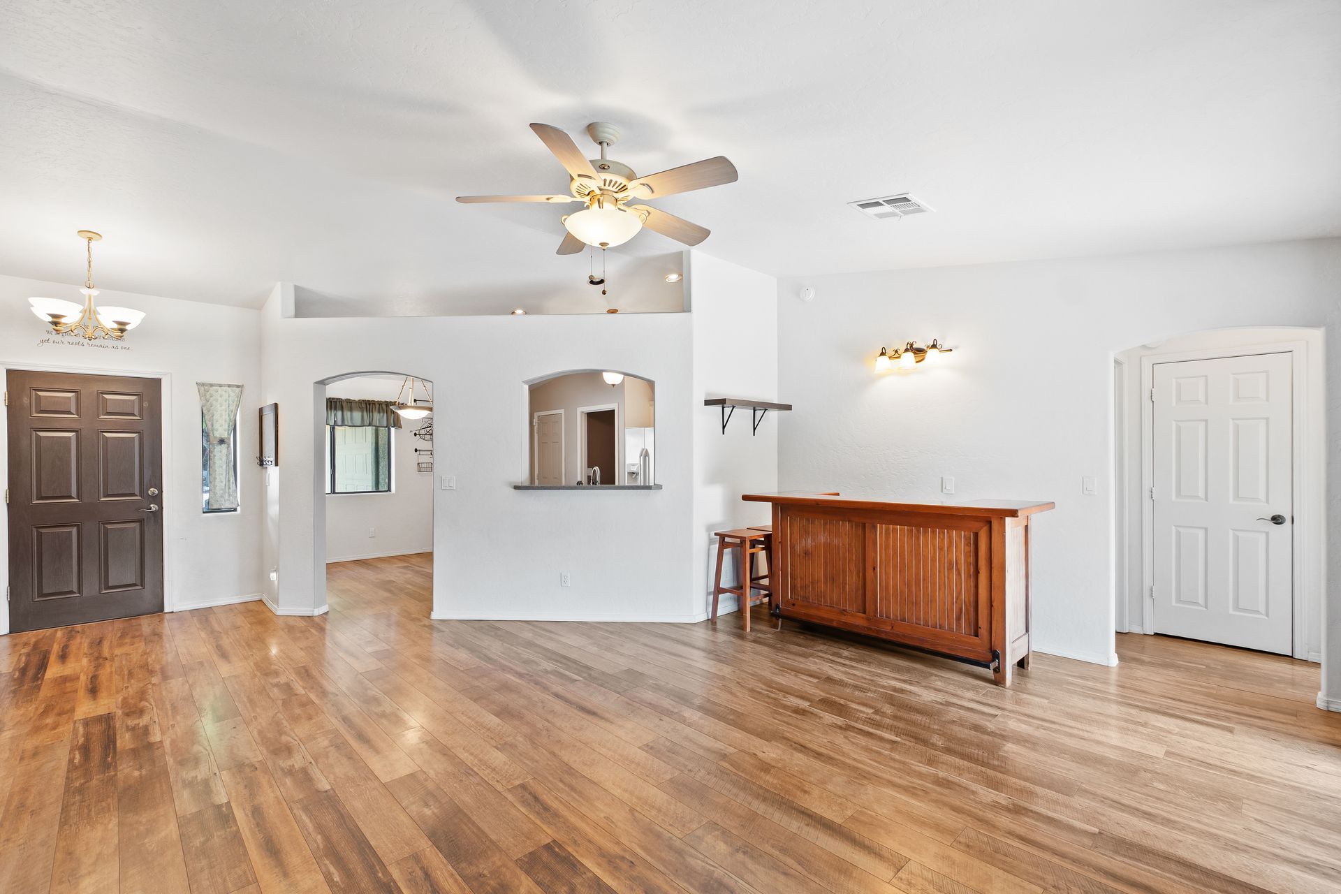 A bright, open-plan room with wood flooring, a ceiling fan, a wooden bar, and two doorways leading to other rooms. A bright, open-plan room with wood flooring, a ceiling fan, a wooden bar, and two doorways leading to other rooms.