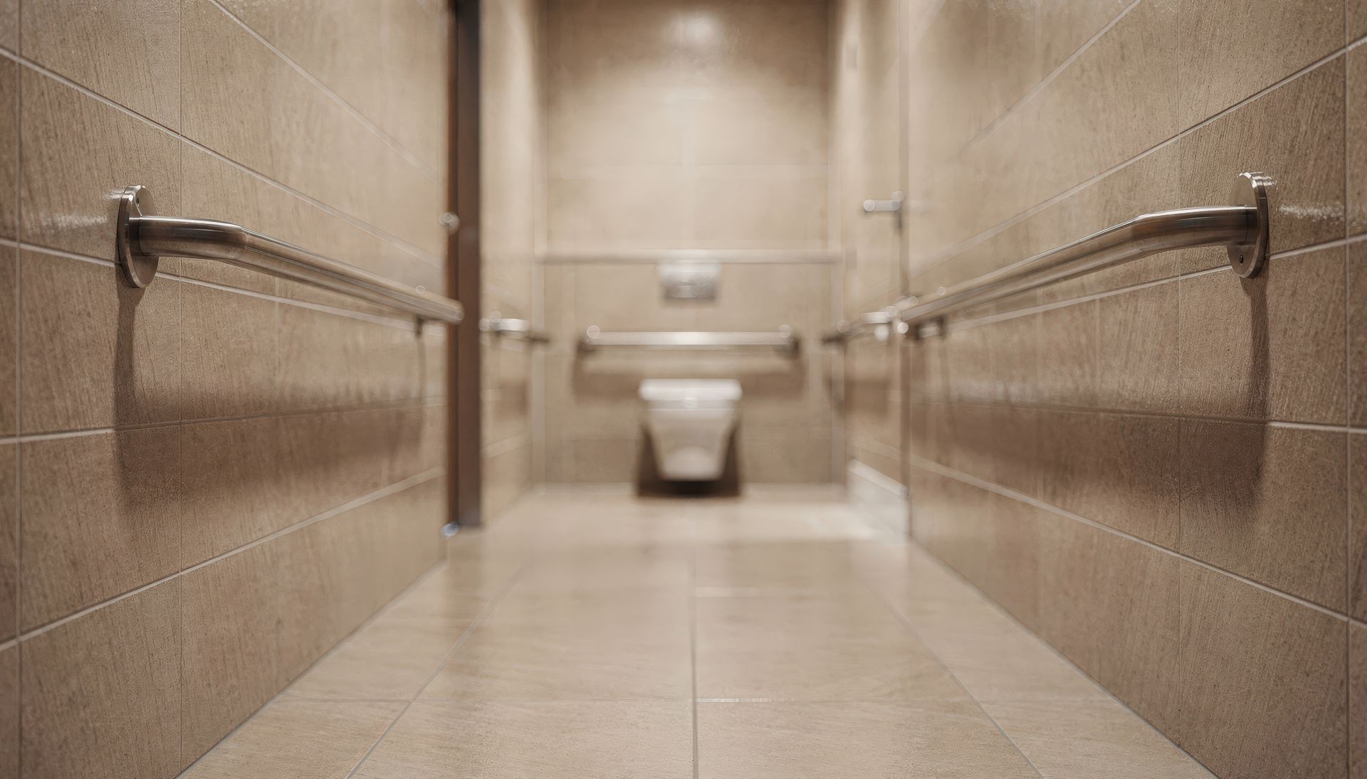 Long hallway of a public restroom with tan tile walls, stainless steel handrails, and a toilet in the distance. Long hallway of a public restroom with tan tile walls, stainless steel handrails, and a toilet in the distance.
