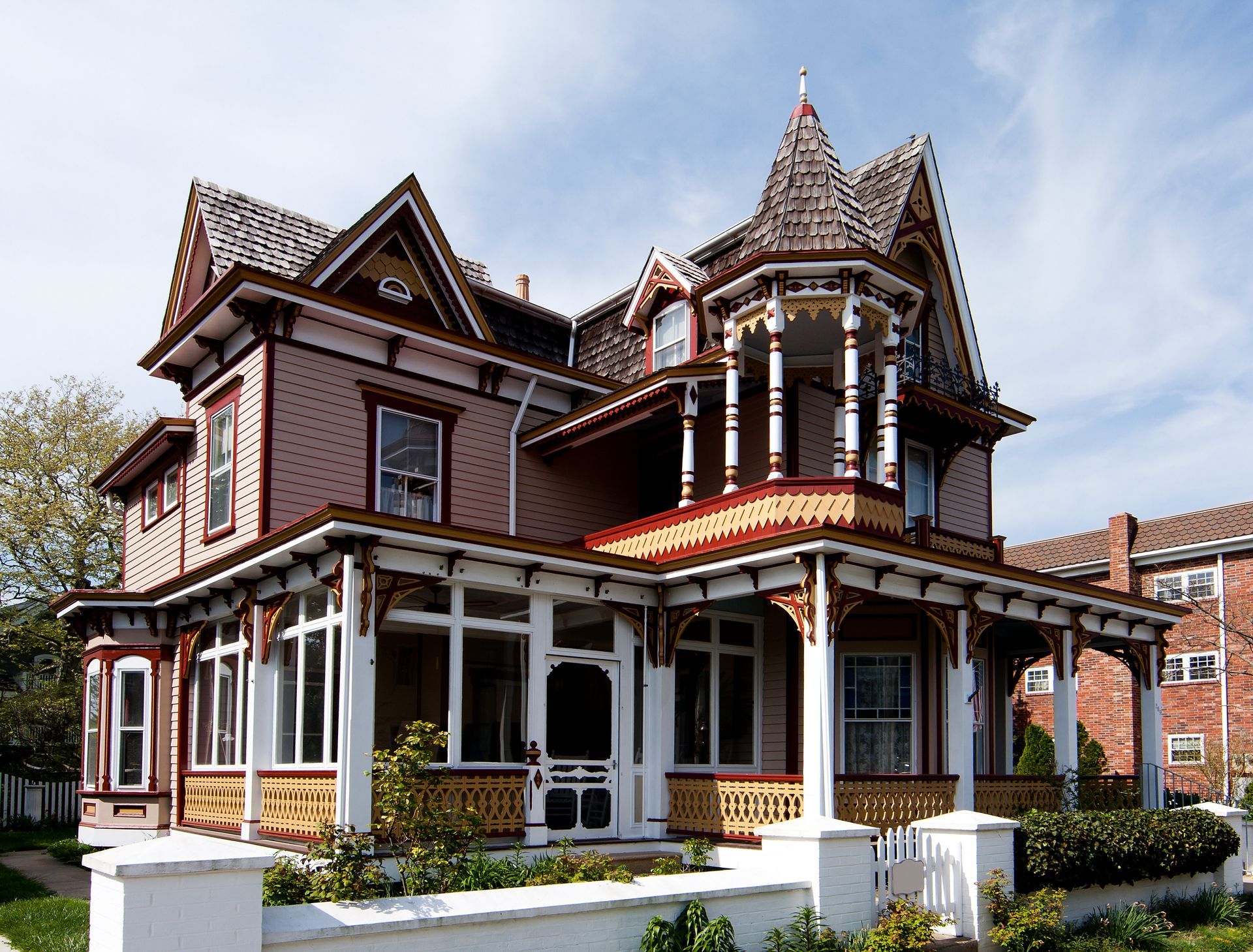 Victorian-style house with pink siding, wrap-around porch, and decorative trim under a blue sky. Victorian-style house with pink siding, wrap-around porch, and decorative trim under a blue sky.