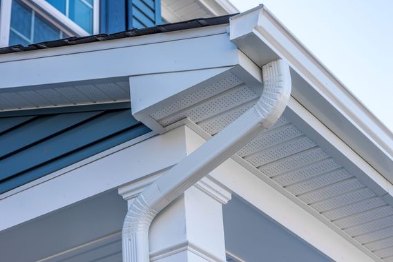 White gutter and downspout on a house with a blue sky background.
