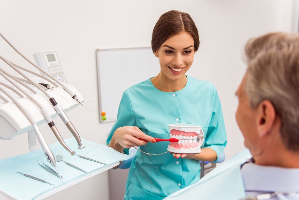 A Female Dentist Is Teaching A Man How To Brush His Teeth — Miami Denture Clinic In Burleigh Heads, QLD