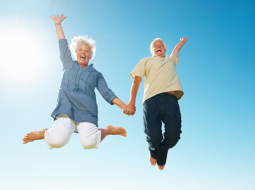 An Elderly Couple Jumping In The Air Holding Hands — Miami Denture Clinic In Burleigh Heads, QLD