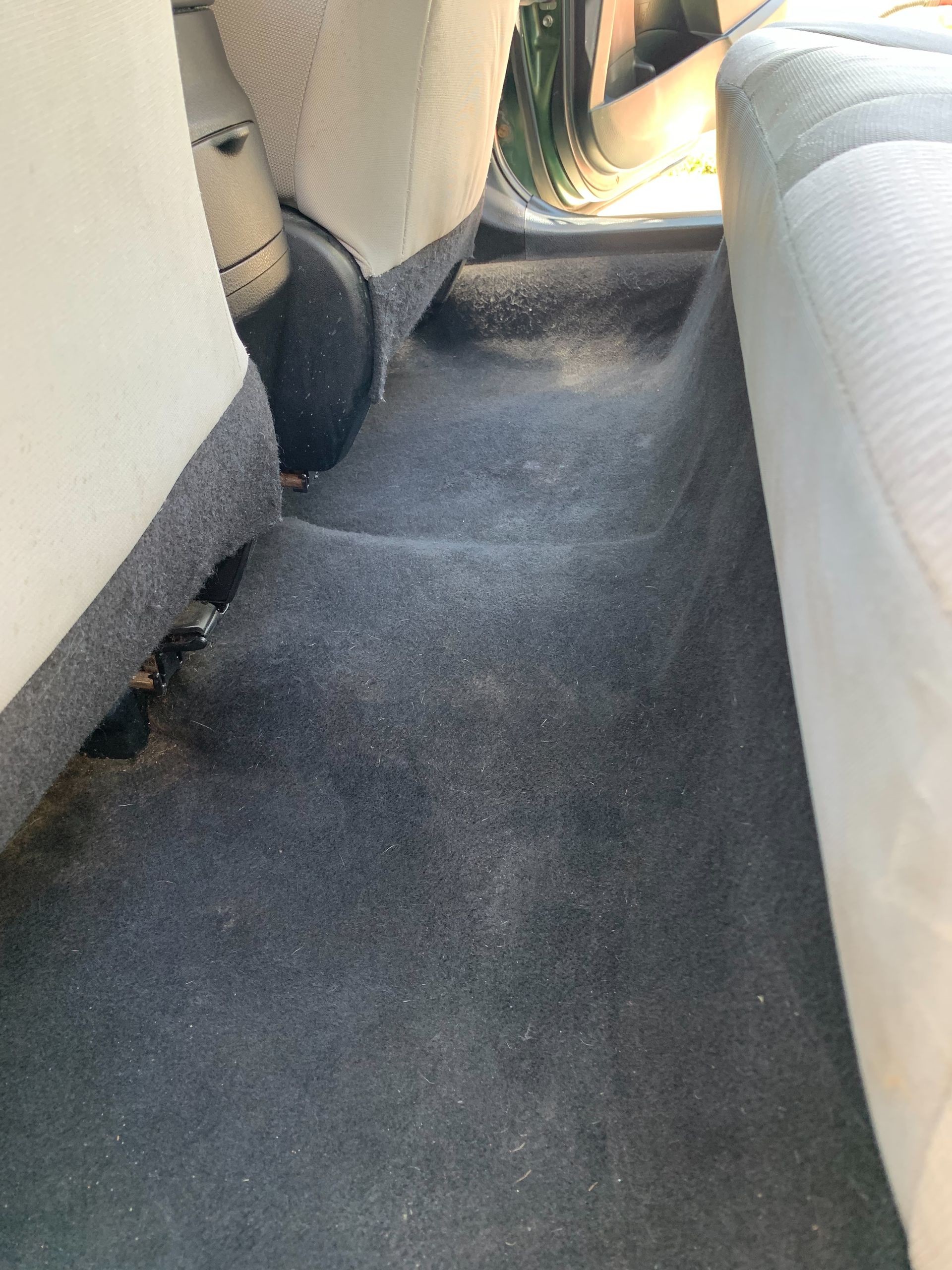 The back seat of a car with a dirty carpet.