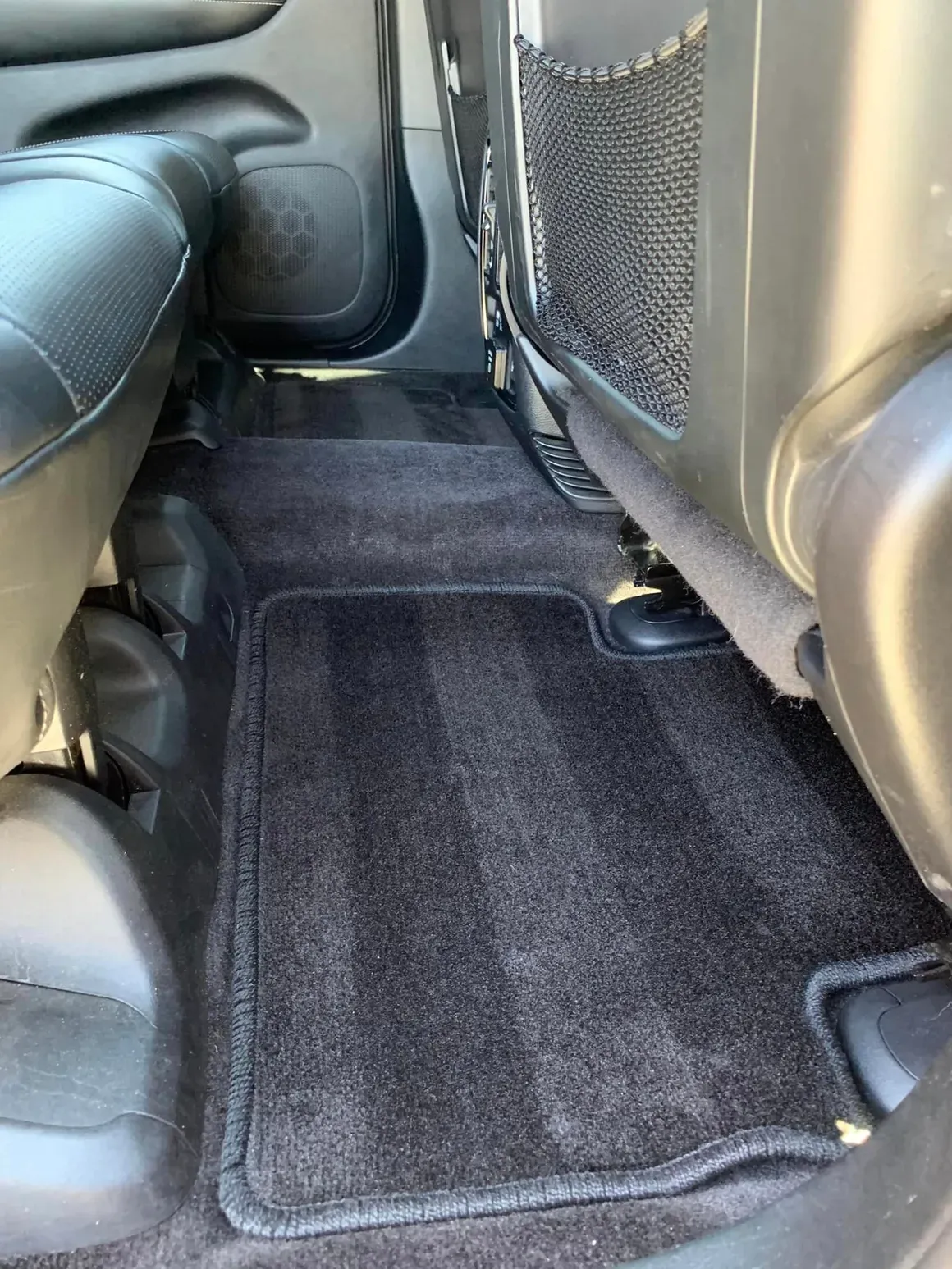 The back seat of a car with a black mat on the floor.