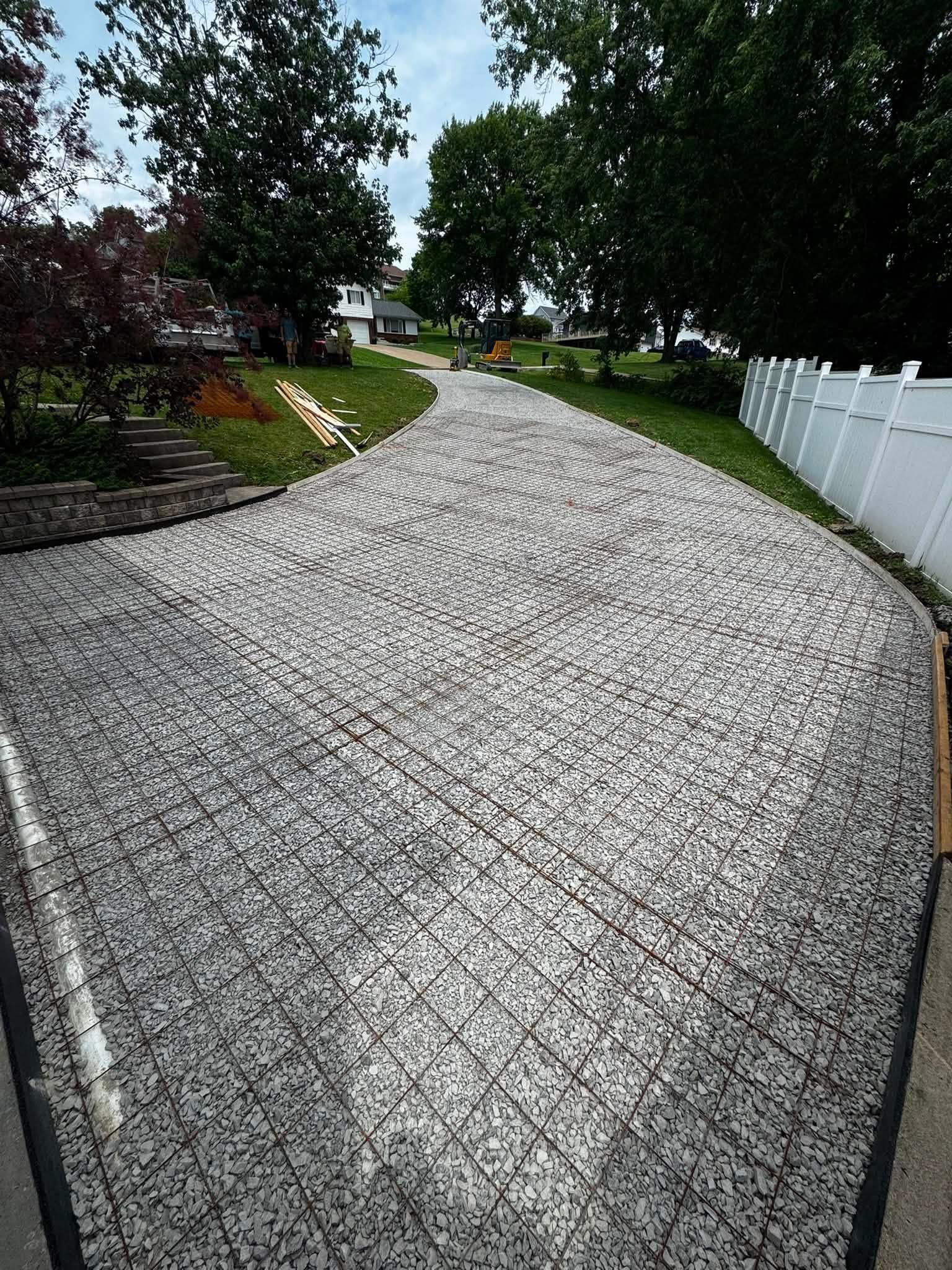 Curved cobblestone driveway beside a white fence and green lawn under trees
