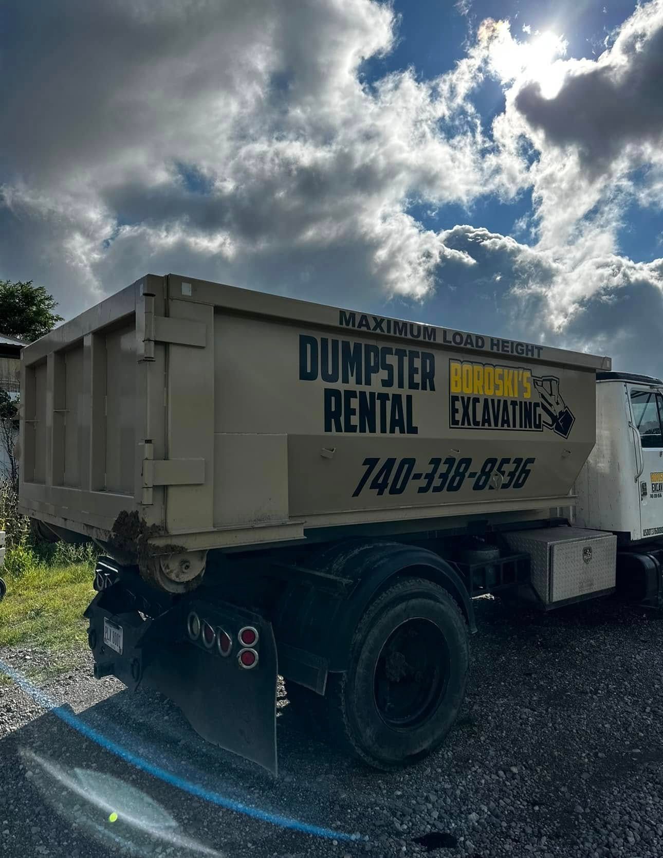 Dumpster rental trailer parked outdoors under a cloudy sky, with company signage on the side.