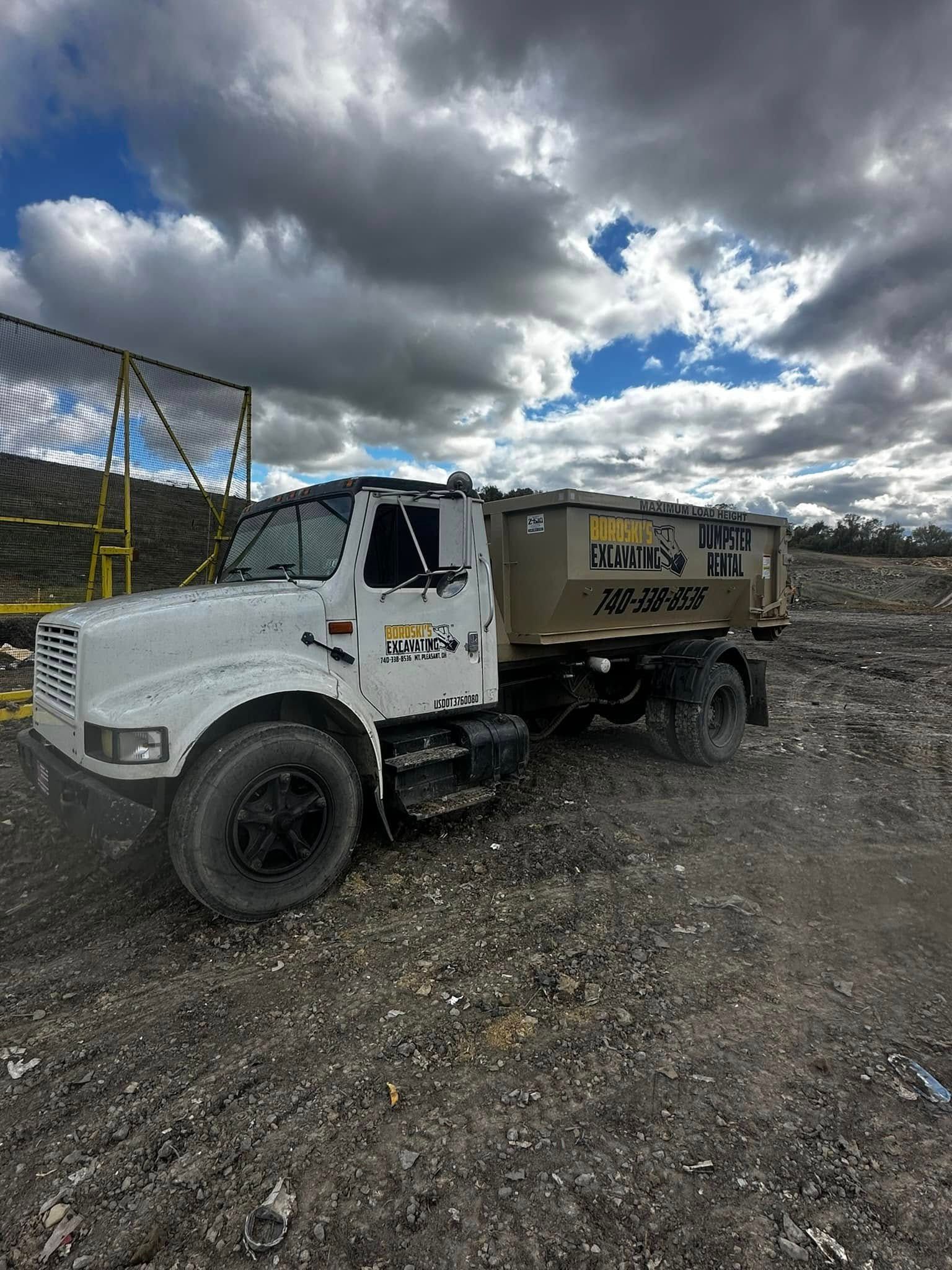 White dump truck parked on a gravel lot under dramatic cloudy sky