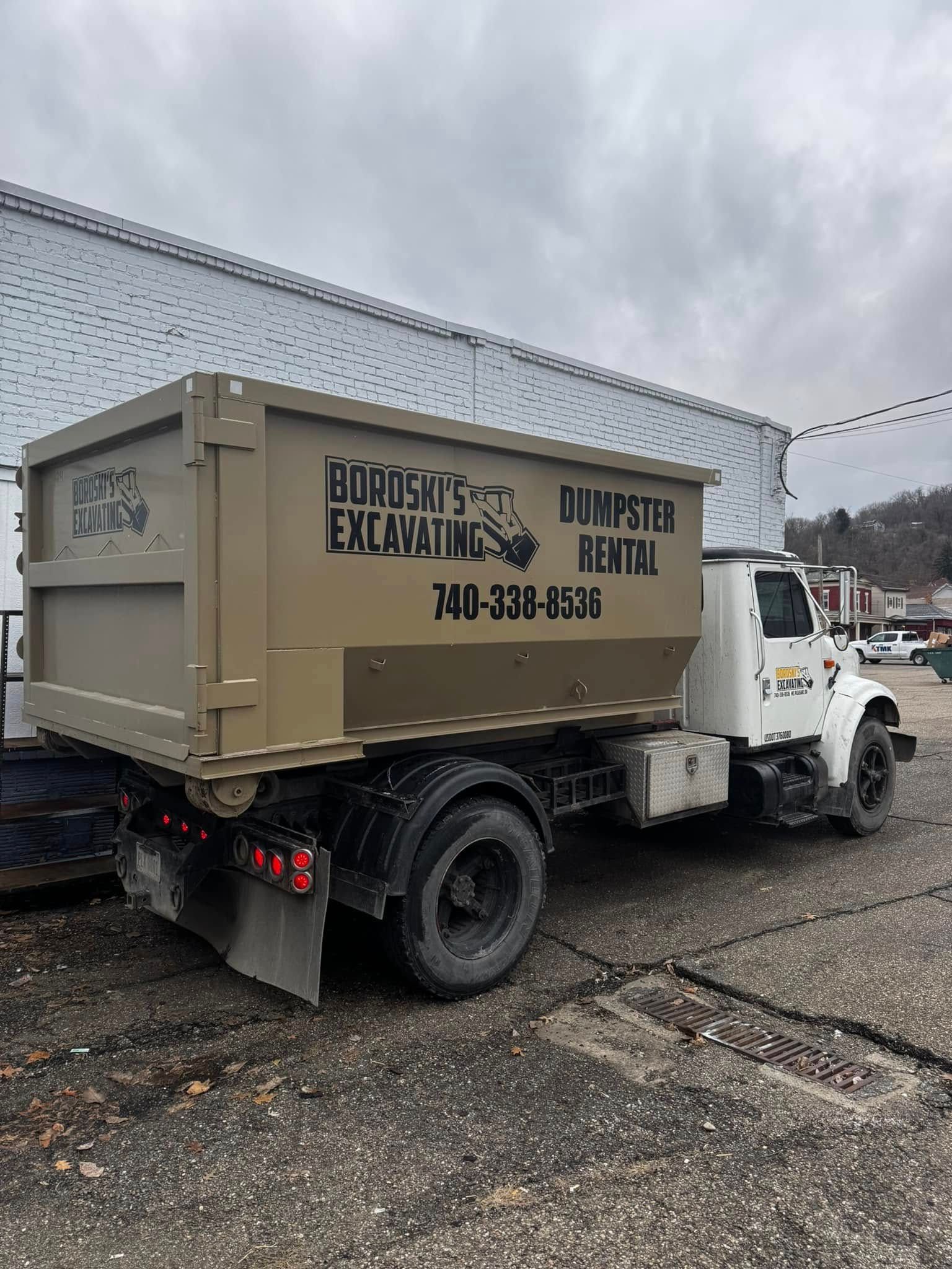 White dump truck with a tan cargo box parked on gravel under a cloudy sky