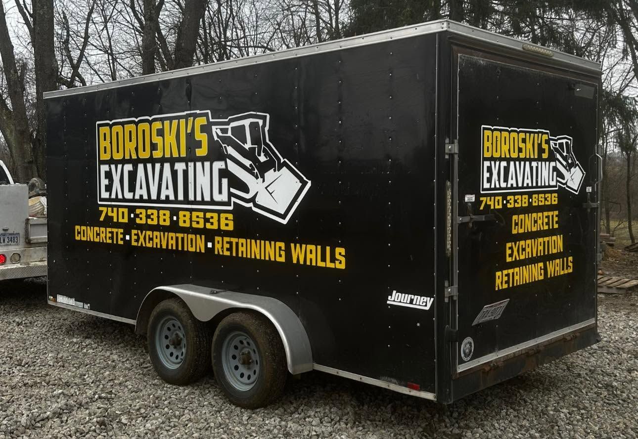 Black Borosh’s Excavating trailer with yellow lettering, parked outdoors on gravel.