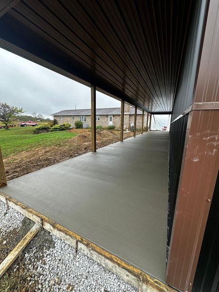Covered concrete walkway beside a grassy yard, with a wooden roof and metal posts.