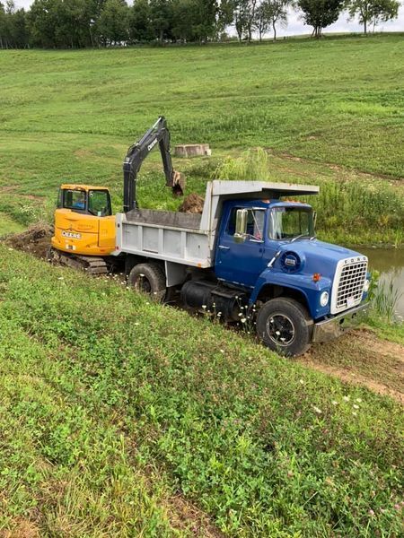 Blue dump truck with yellow excavator loading dirt in a grassy field