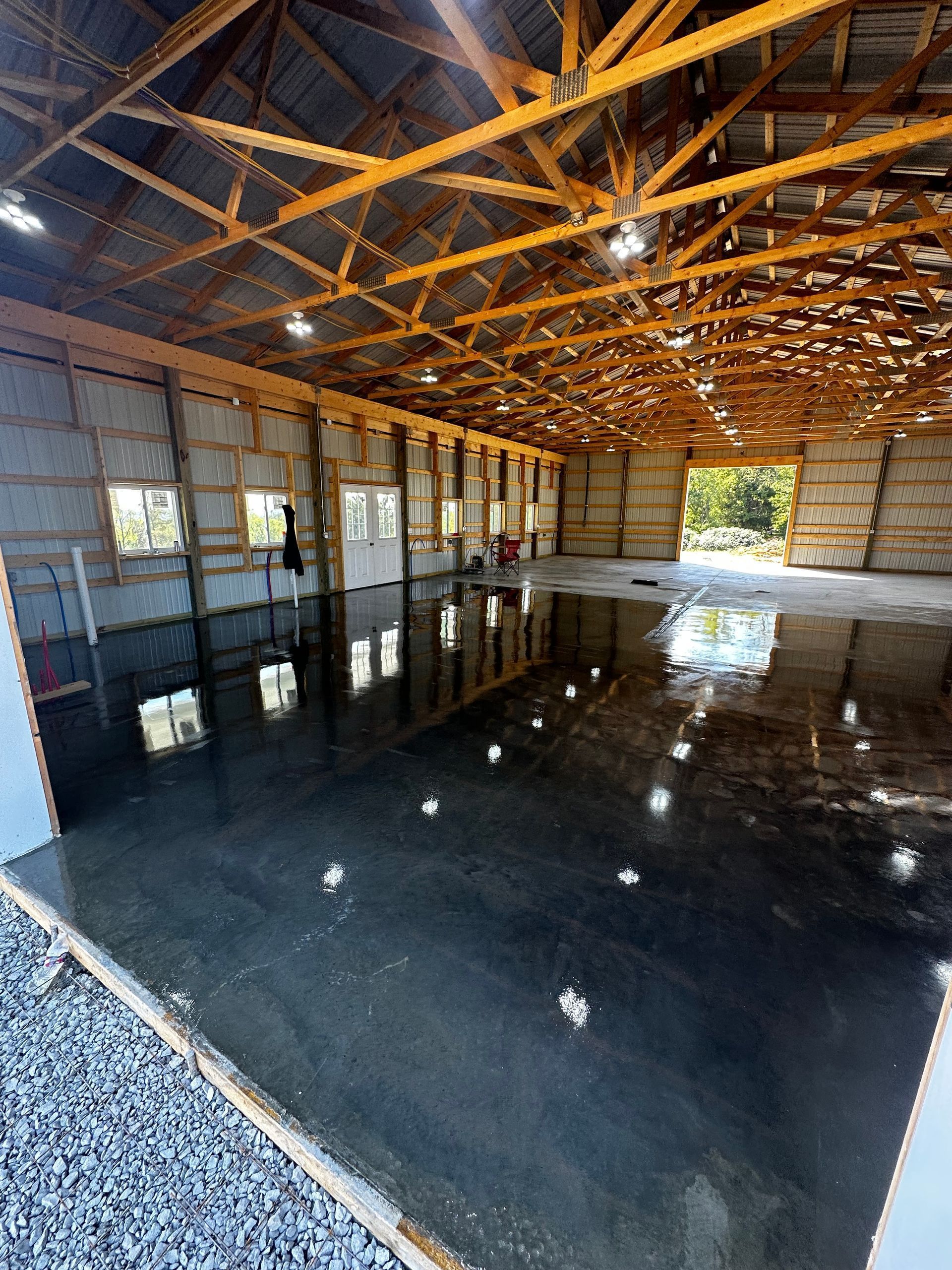 Empty industrial warehouse interior with a glossy black floor and exposed wooden roof trusses.