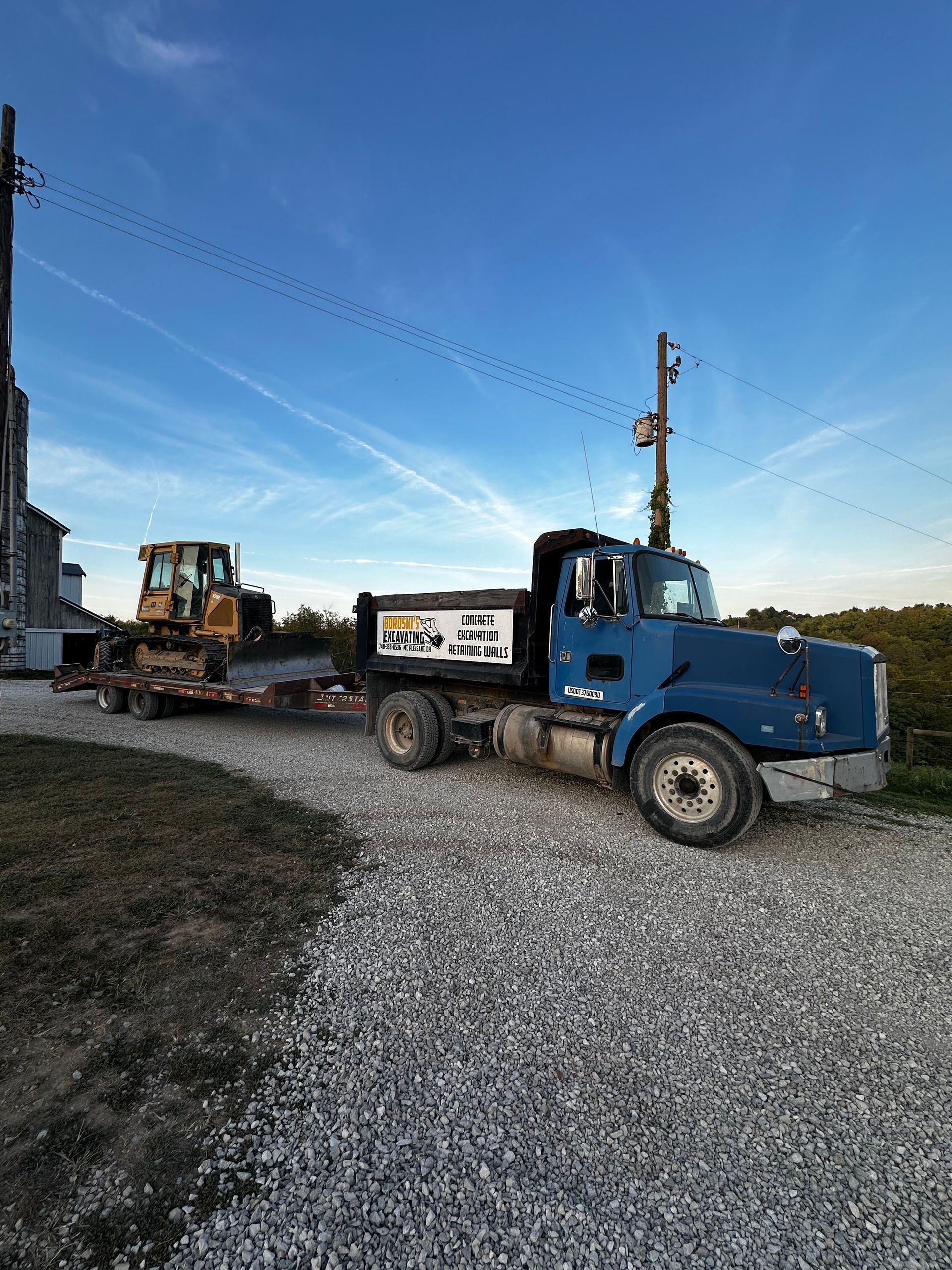 Blue dump truck on a gravel lot with construction equipment and a clear sky at sunset