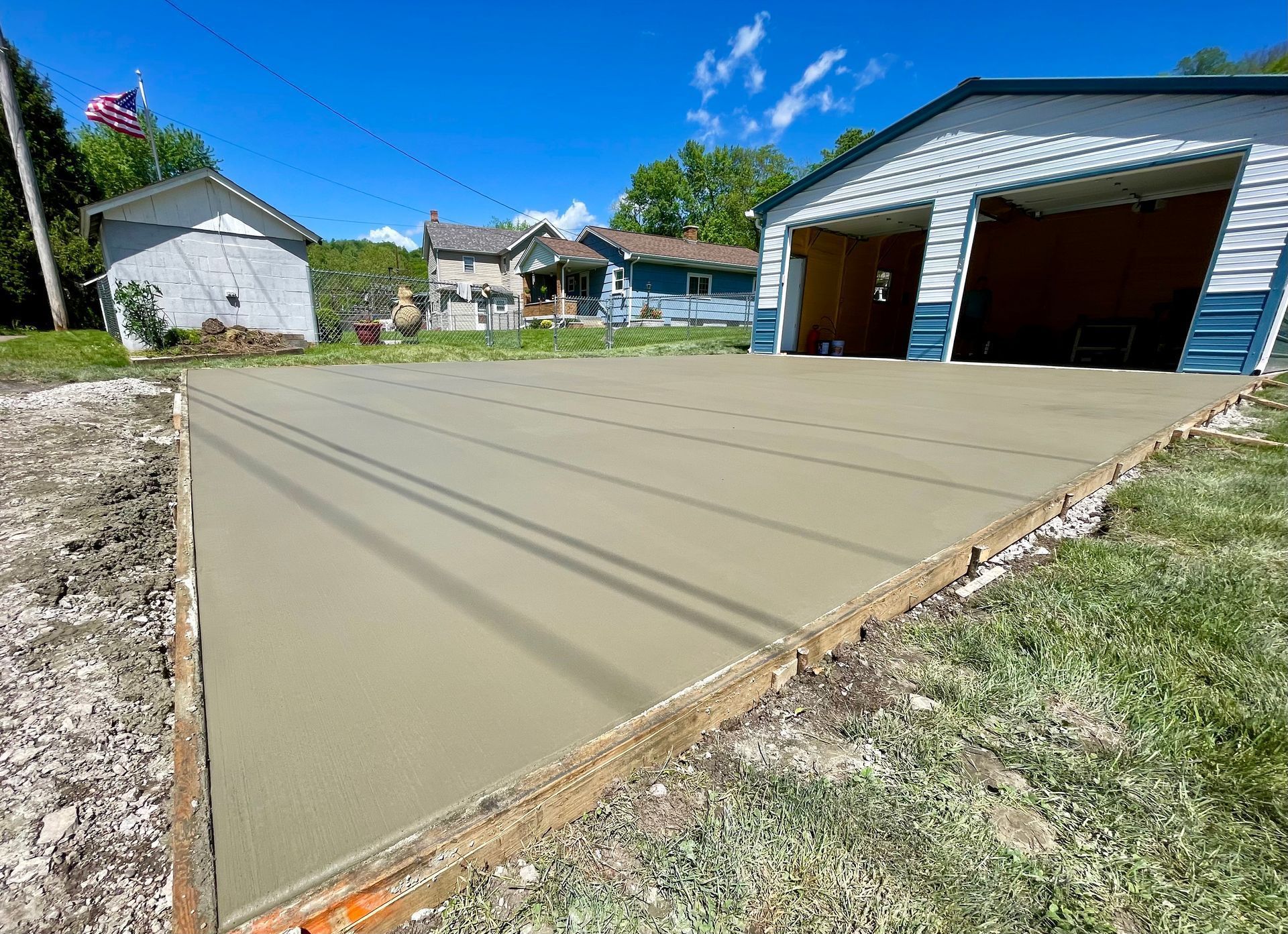 Freshly poured concrete driveway beside a blue garage in a residential yard under a bright sky