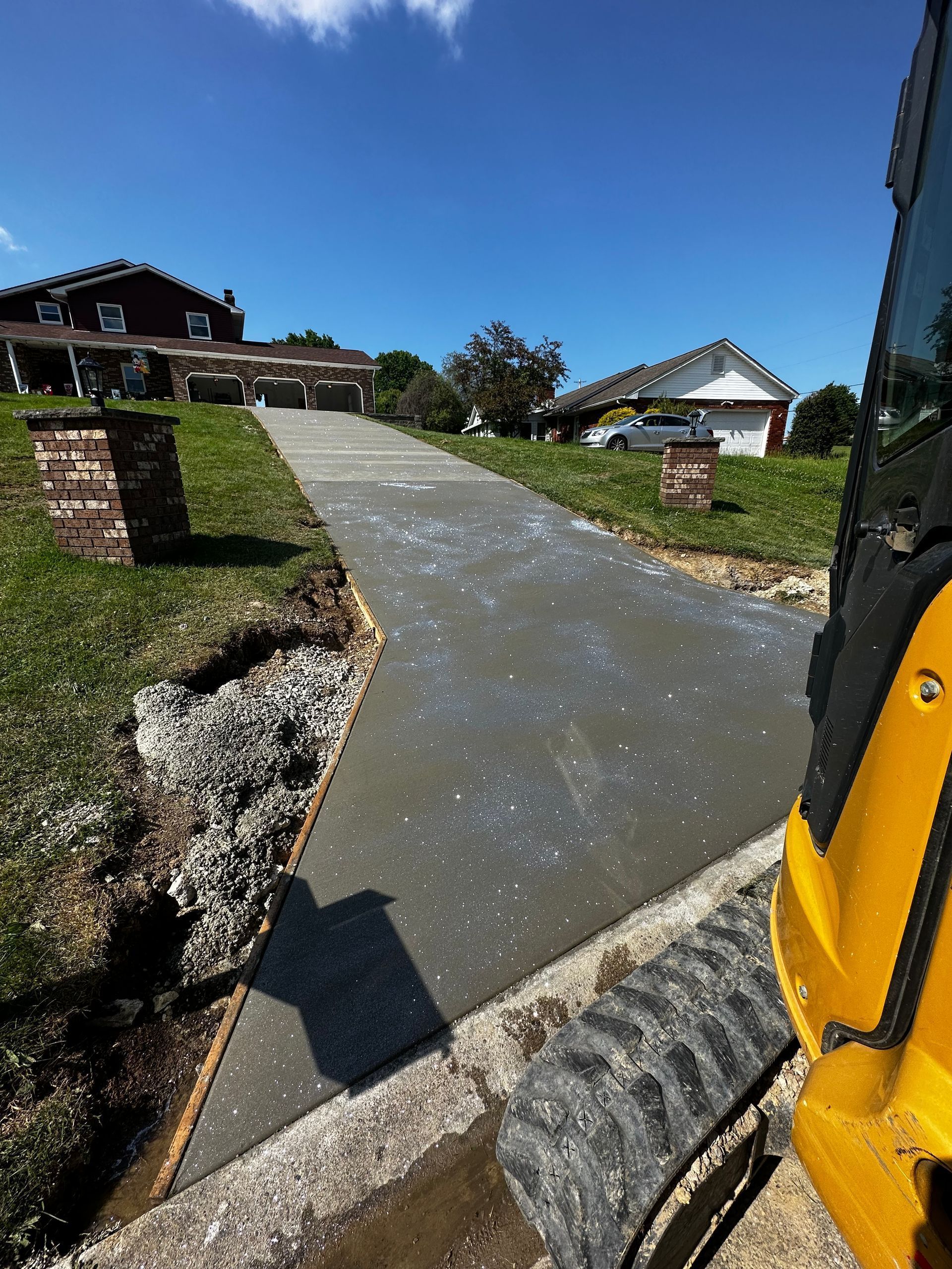 Steep driveway beside houses on a sunny day, viewed from a yellow vehicle.